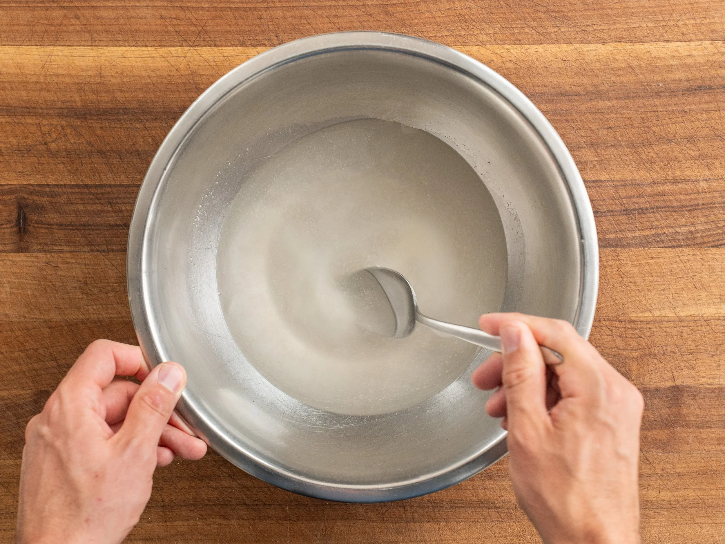 adding yeast to water in metal bowl and stirring with metal spoon