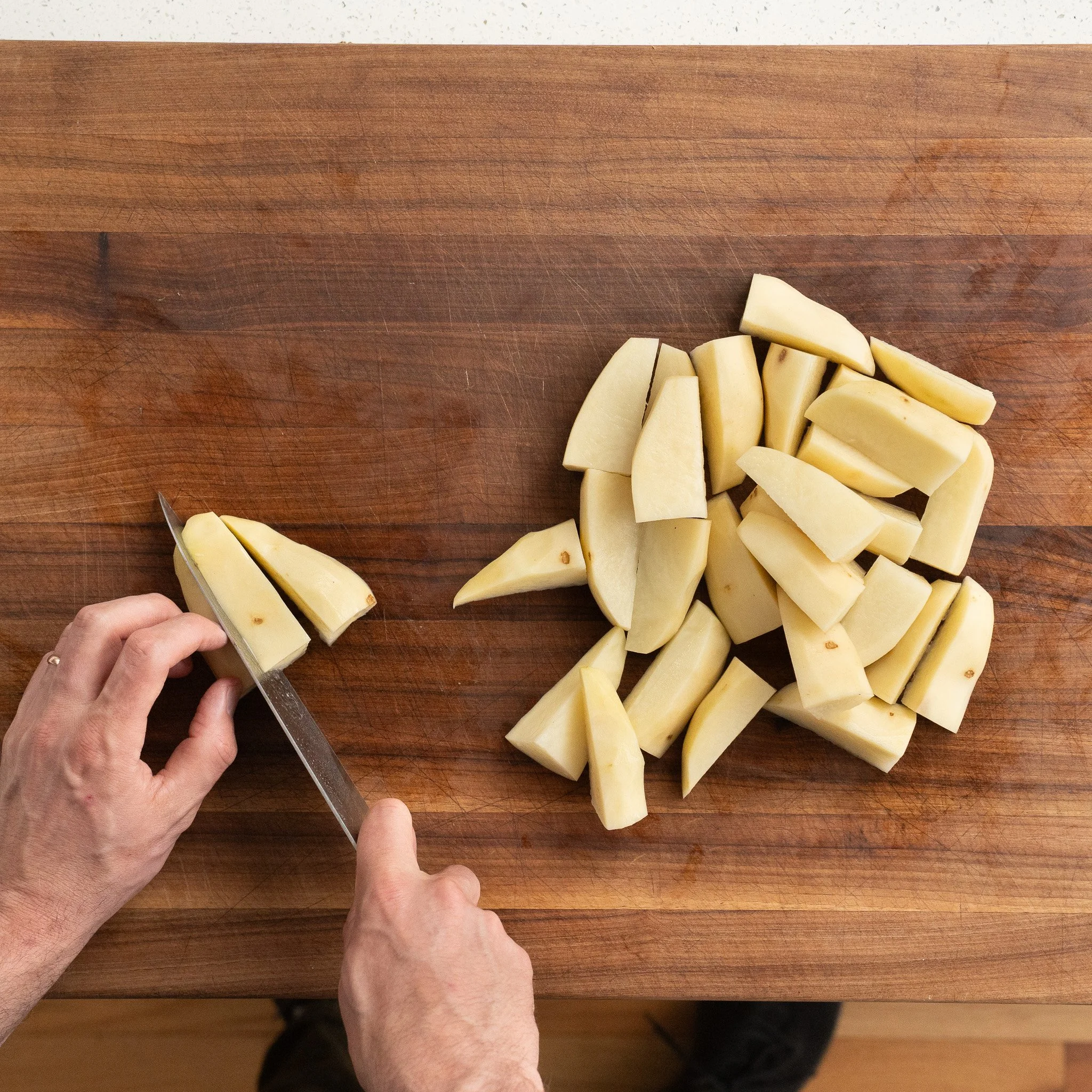 cutting russet potatoes into wedges on a wooden cutting board