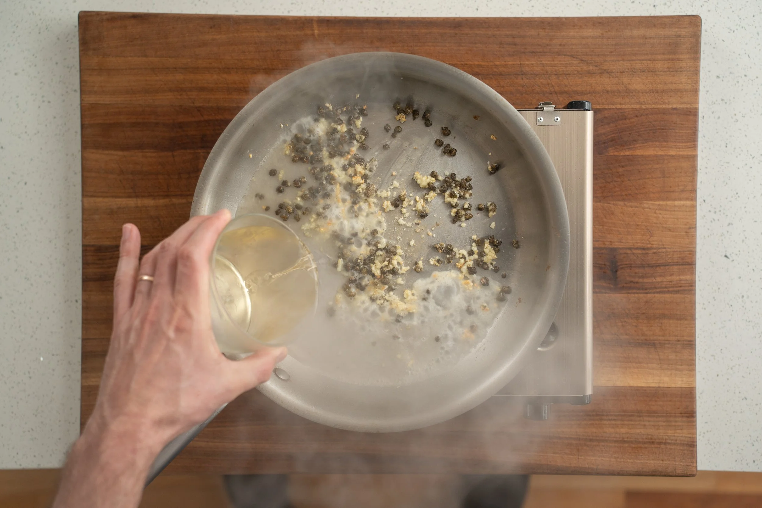 adding white wine to garlic and capers in pan