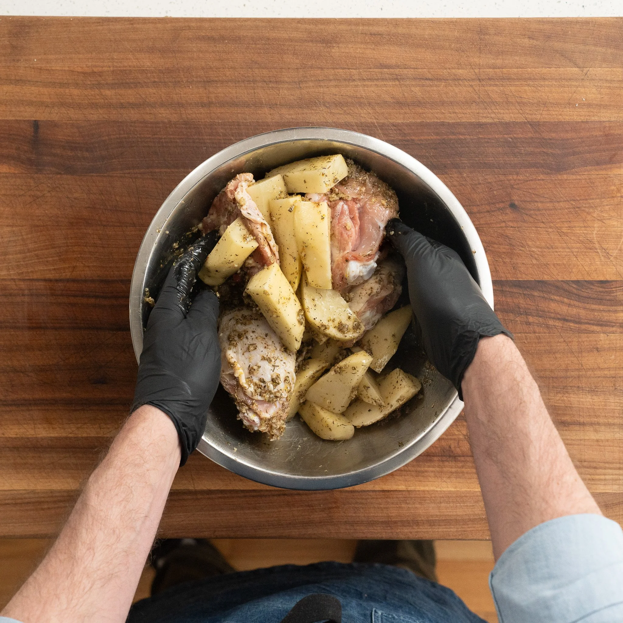 tossing chicken thighs and potatoe wedges with greek marinade in a metal bowl