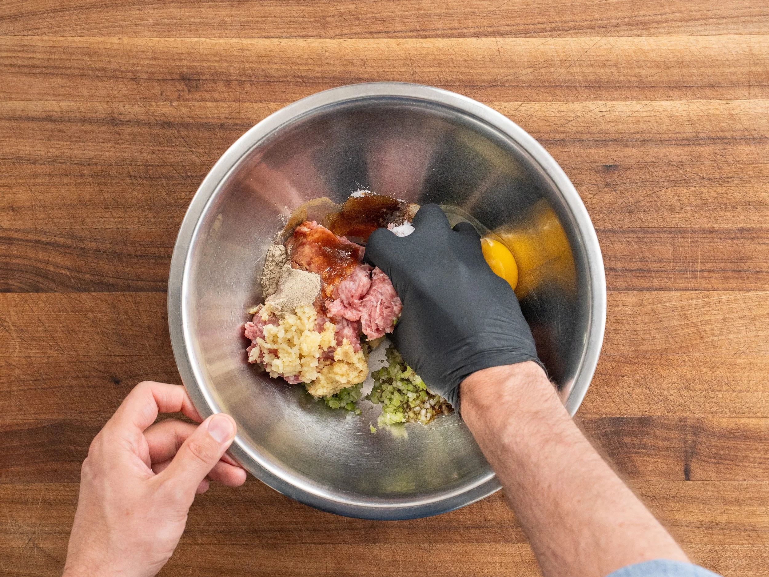 gloved hand mixing wonton filling in a silver bowl