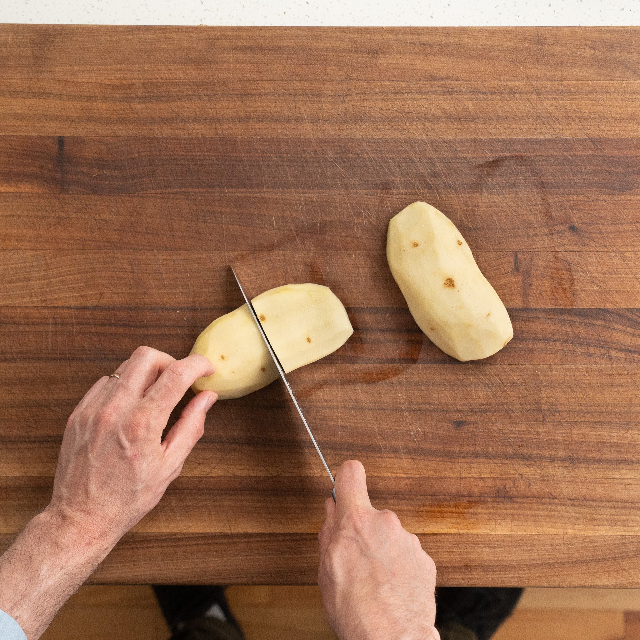 cutting russet potato in quarters on a wooden cutting board