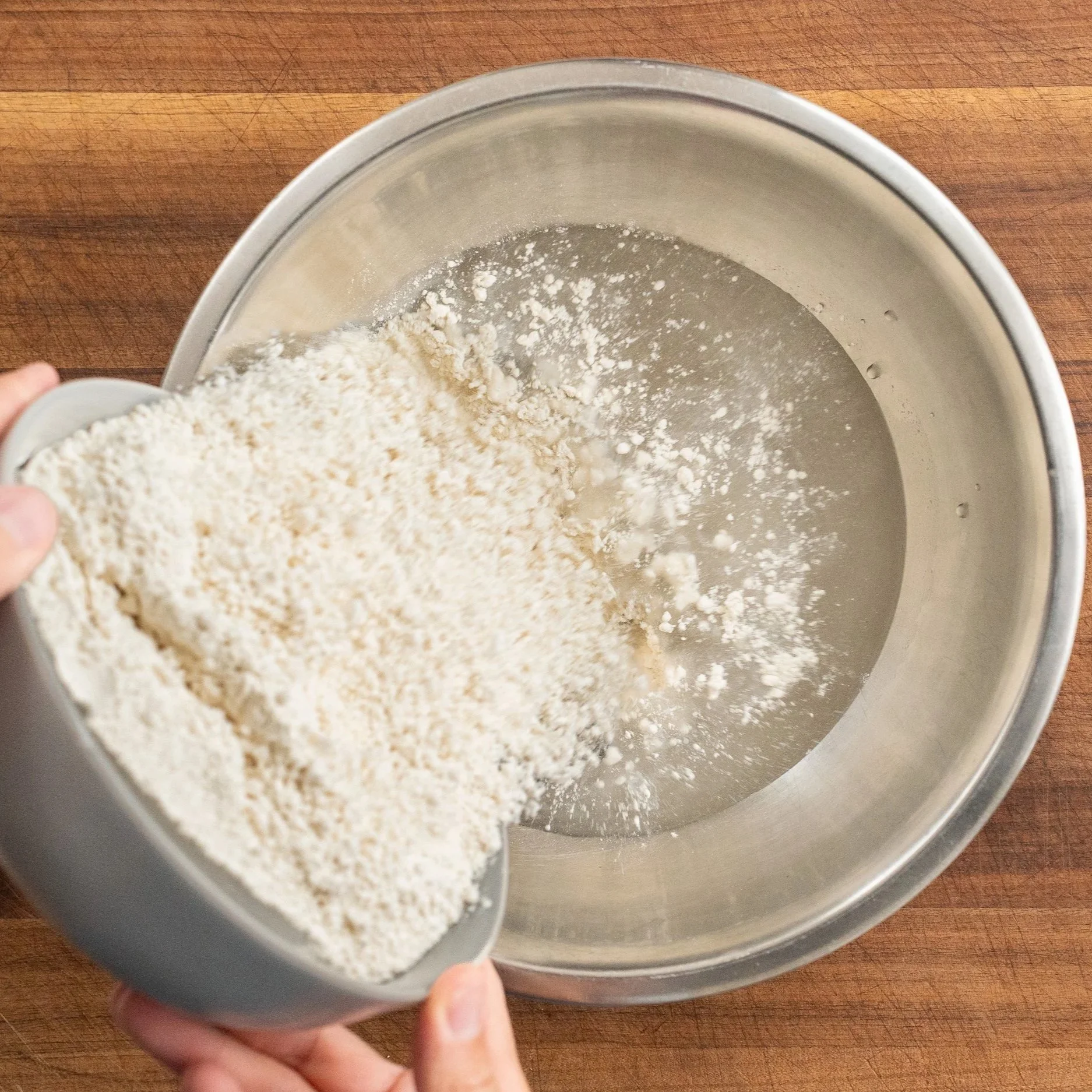 adding flour to metal bowl filled with yeast water