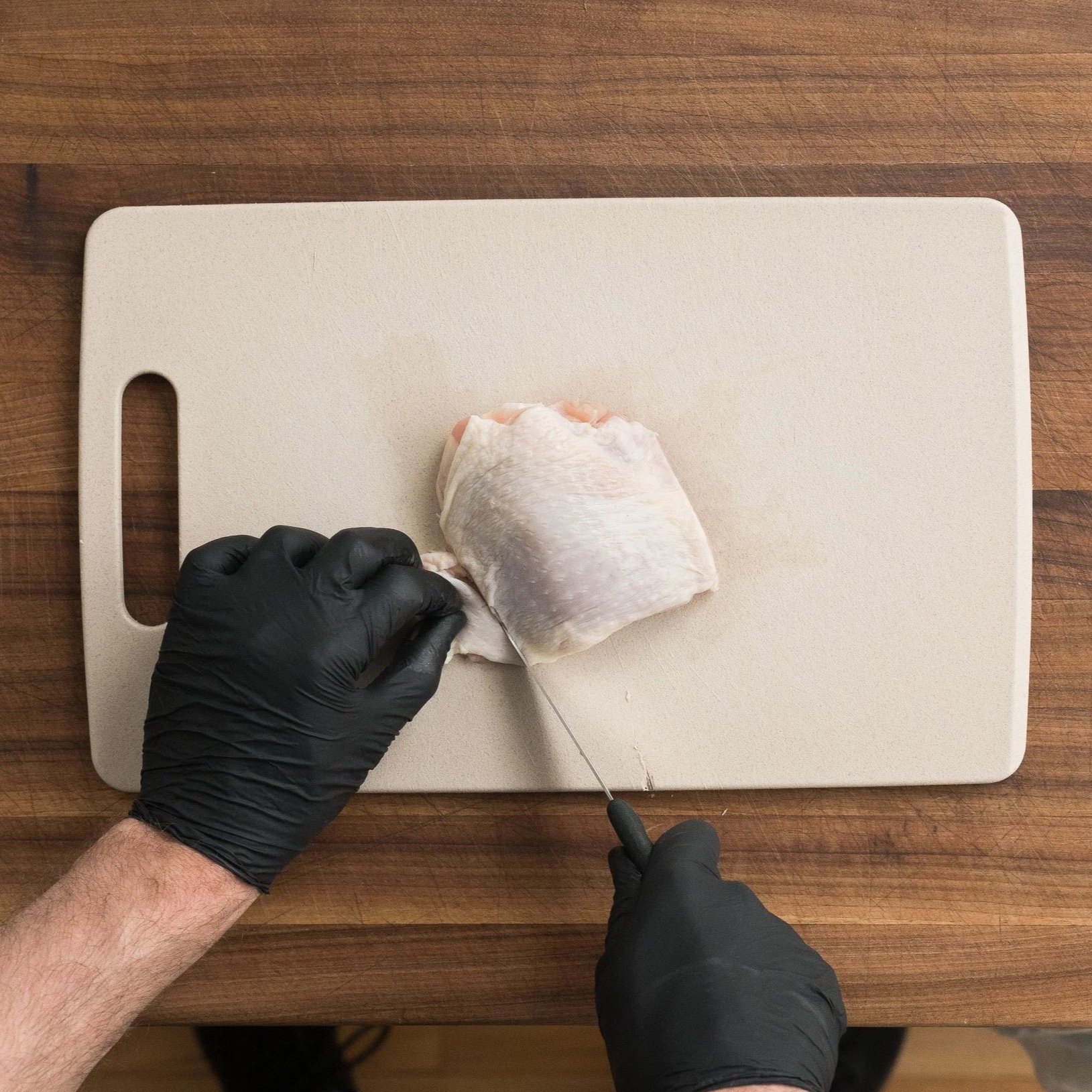 trimming excess skin off a chicken thigh with a sharp knife