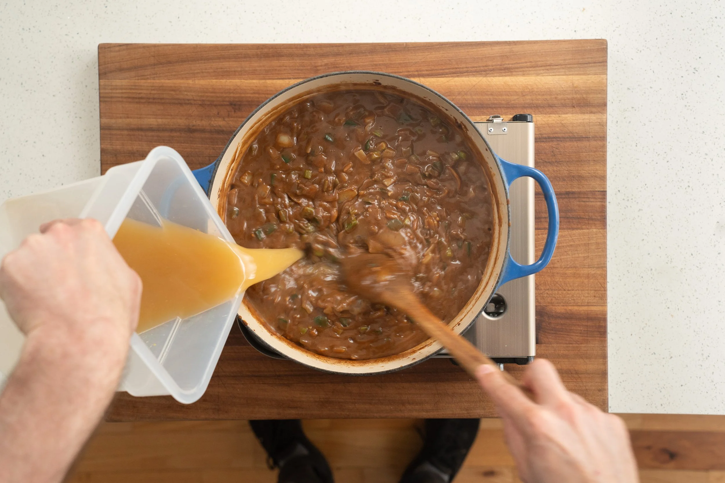 adding chicken stock to a gumbo base in a blue dutch oven