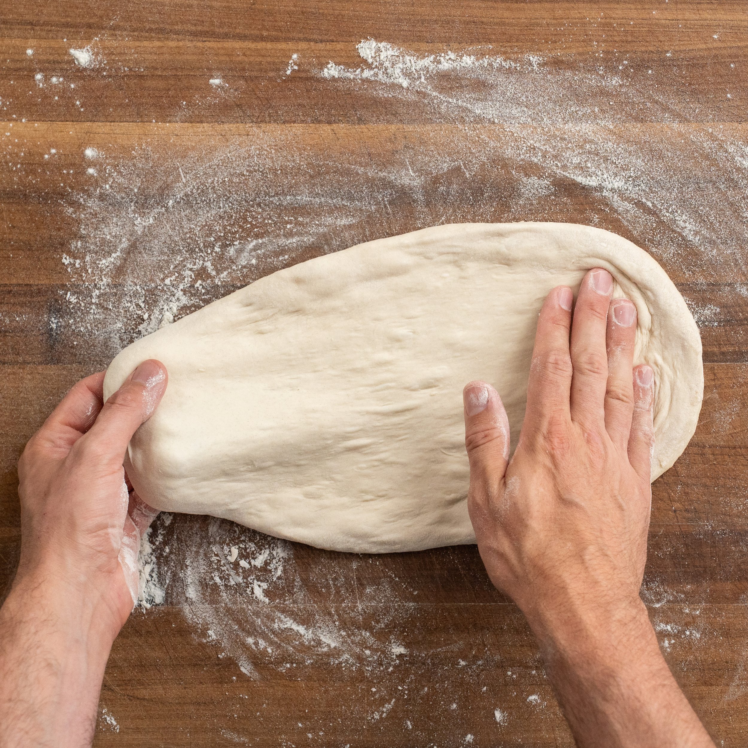 hand stretching pizza dough on wooden cutting board