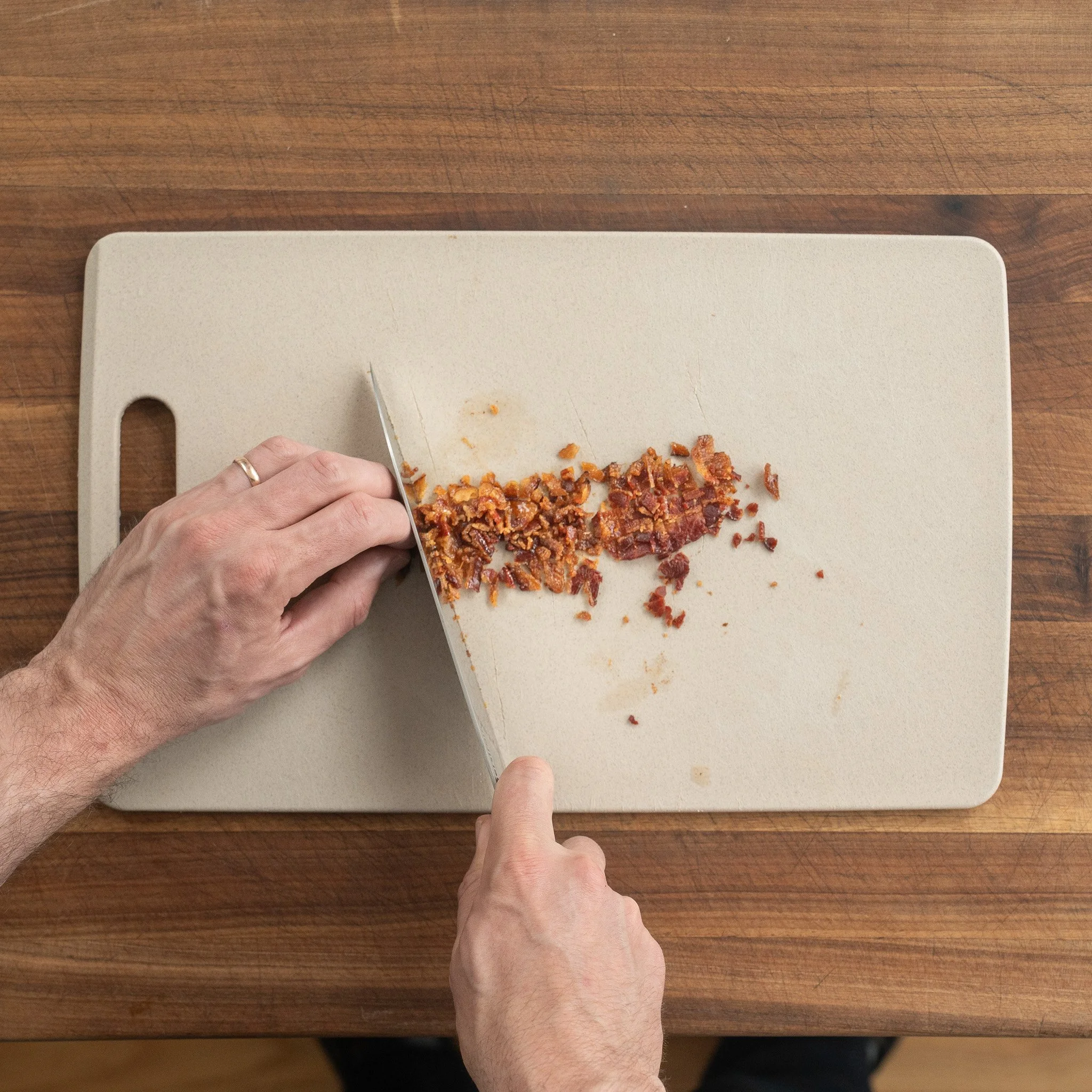 dicing cooked bacon on brown cutting board