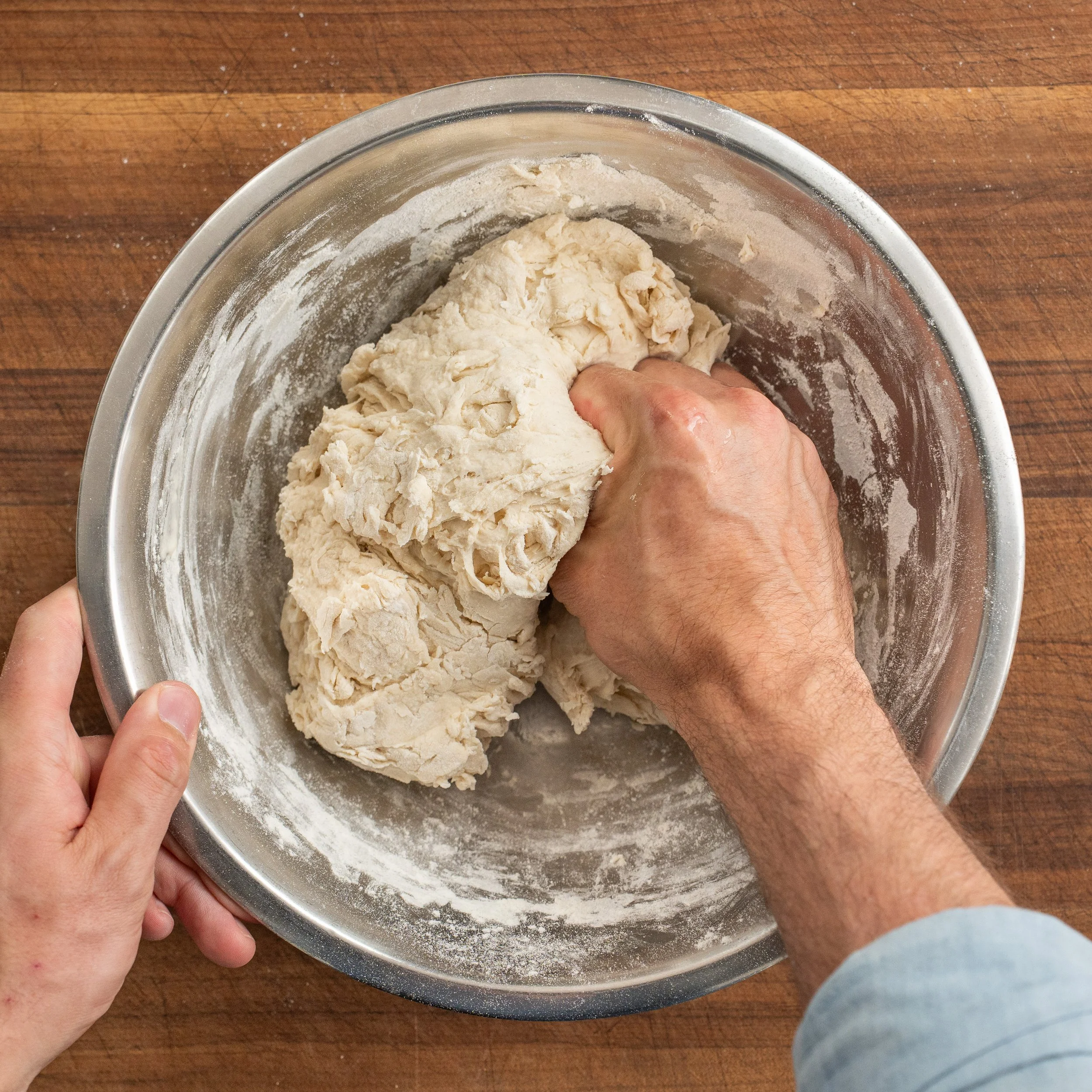 man's hand squeezing shaggy dough ball in metal bowl