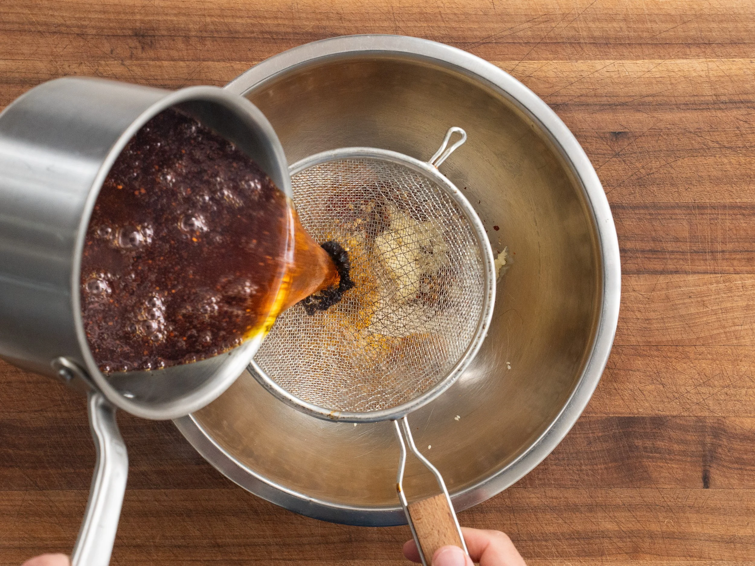 pouring red oil into a strainer on top of a silver bowl