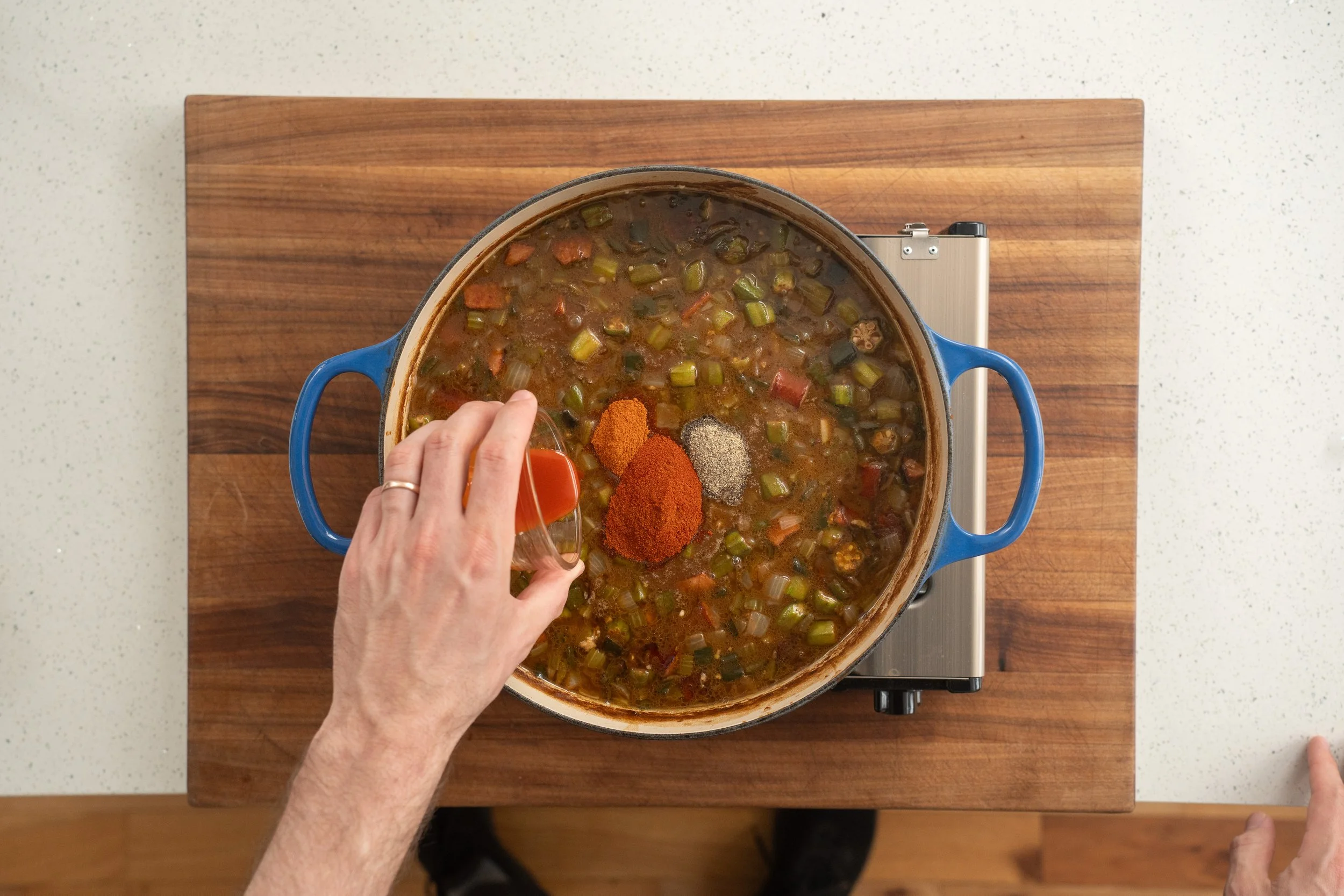 adding spice blend to gumbo in a blue dutch oven