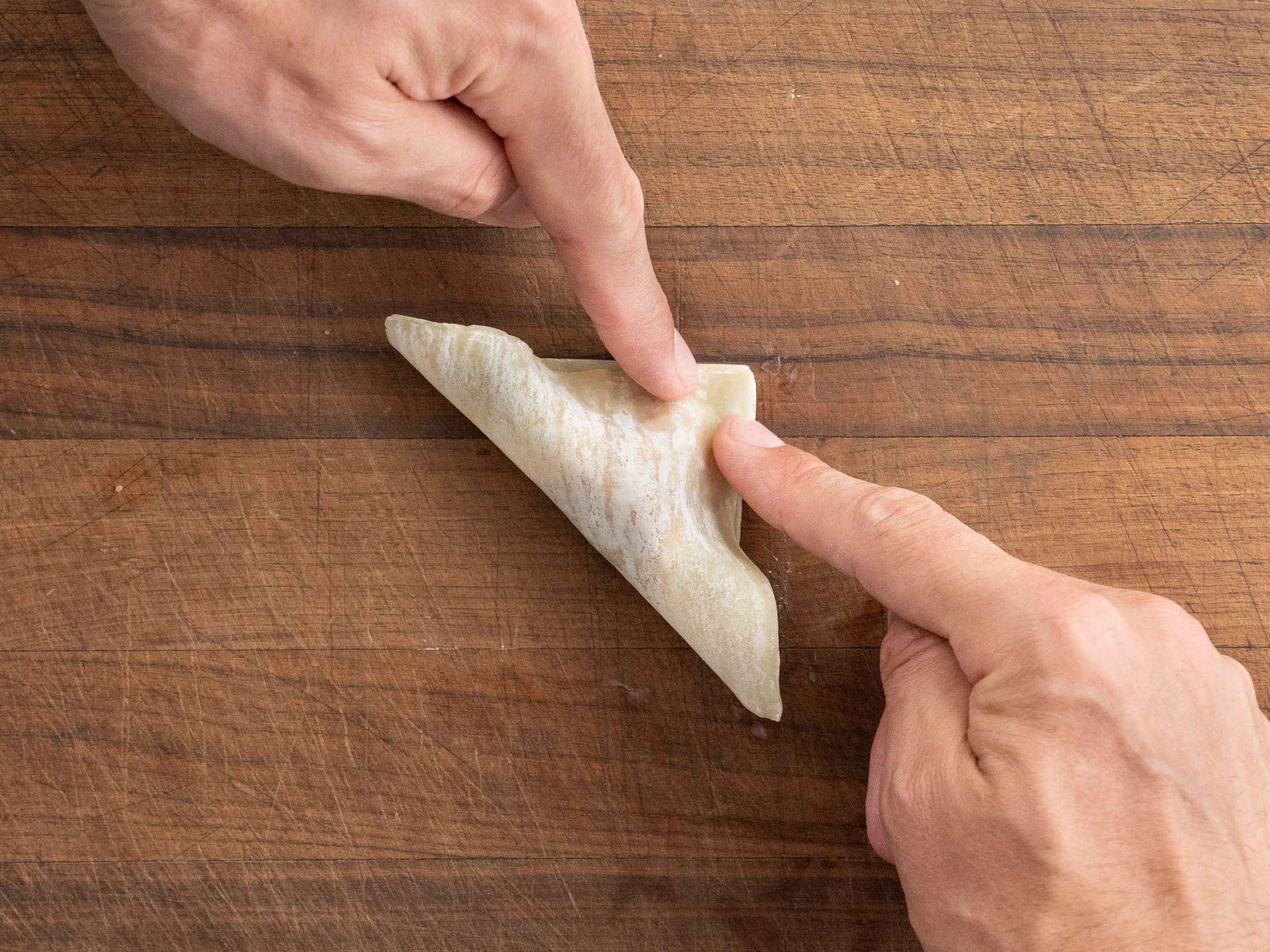 two fingers pressing a wonton wrapper together on a cutting board