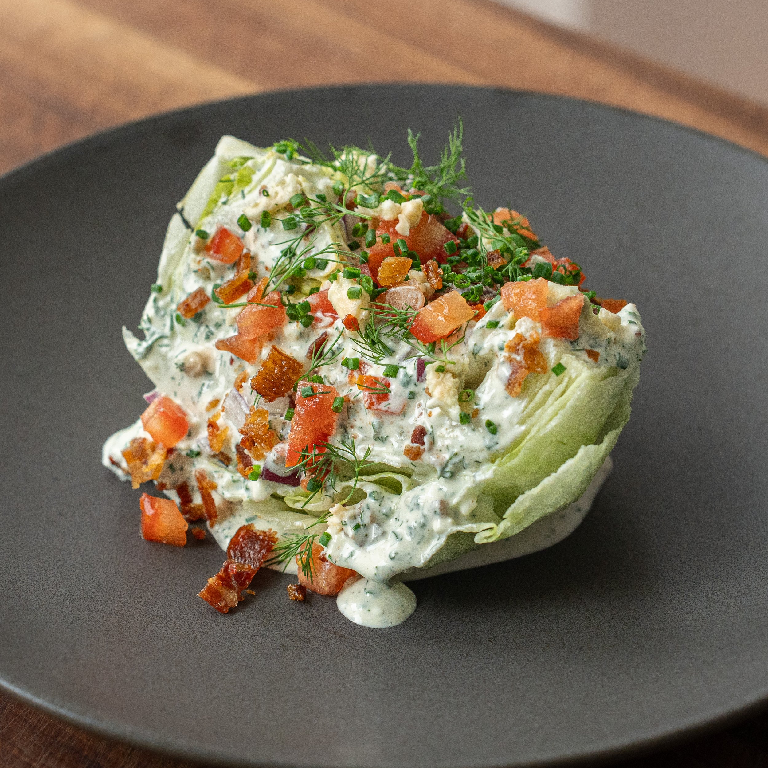 classic wedge salad with bacon tomato and blue cheese on a charcoal plate