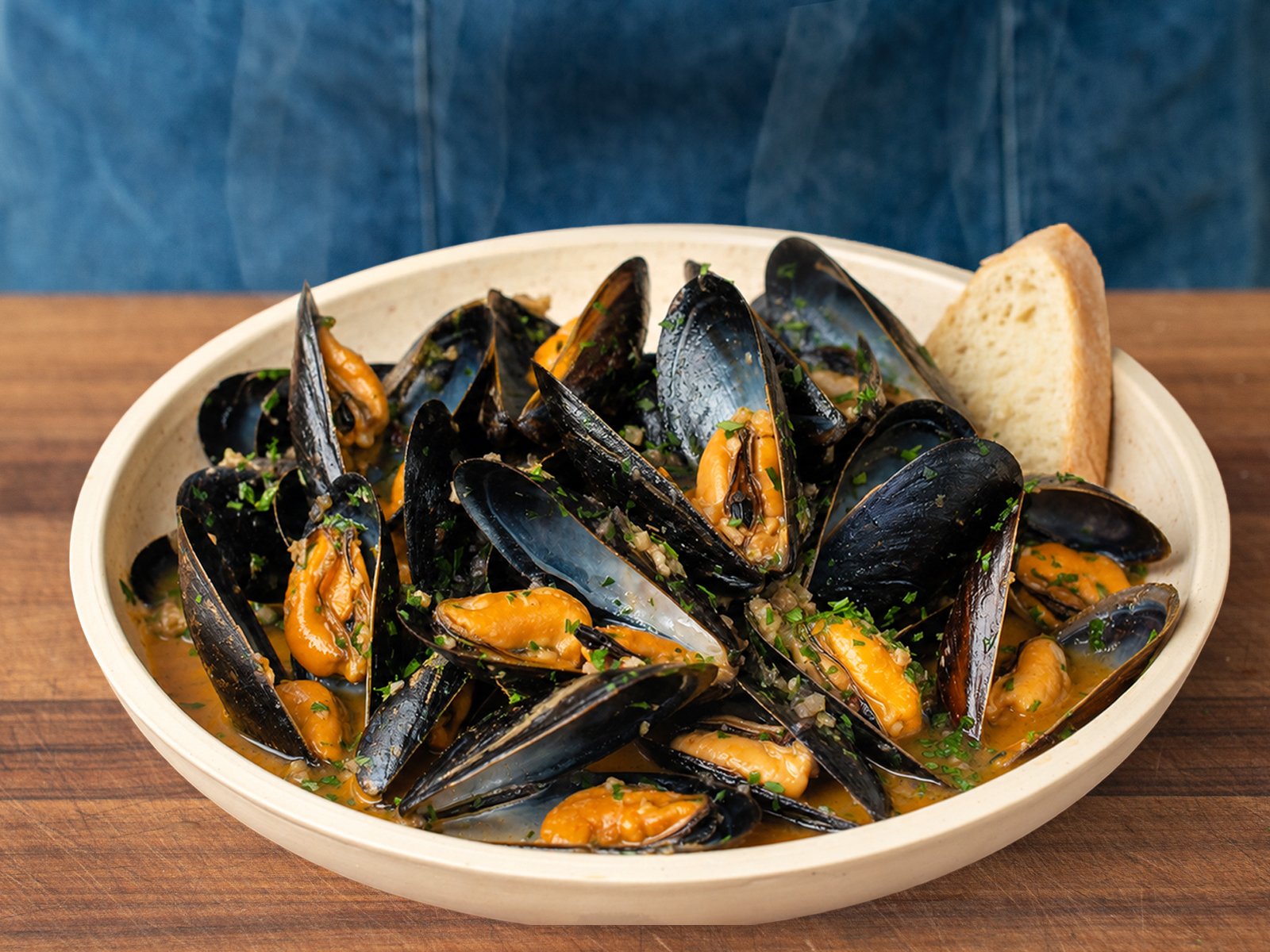 bowl of finished mussels in white wine sauce garnished with chopped parsley and bread