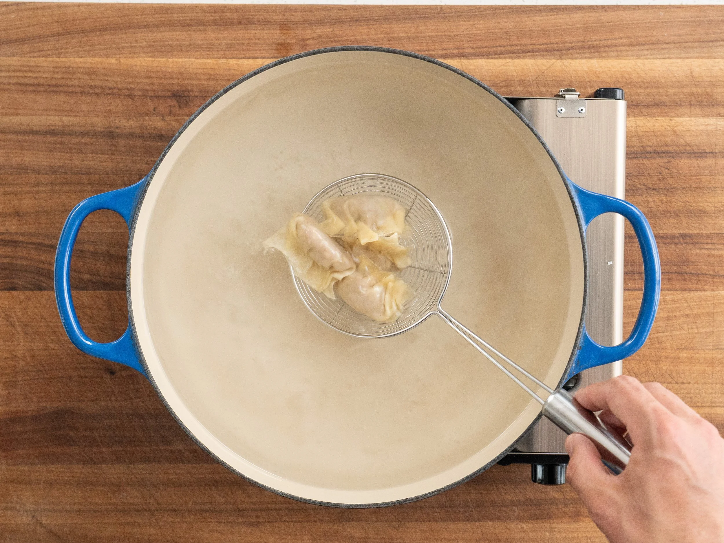 dropping wontons into blue dutch oven with a silver strainer