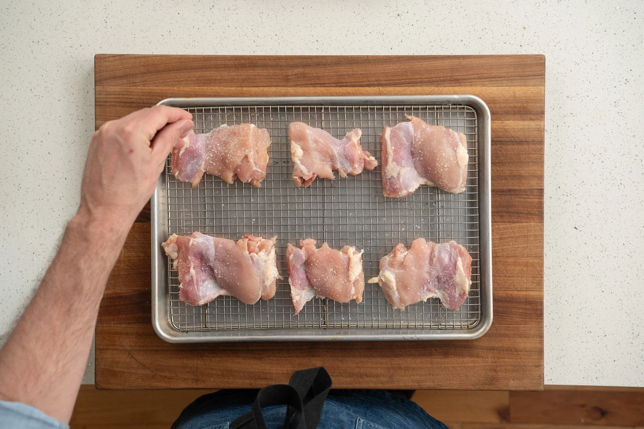applying salt to chicken thighs on a silver sheet tray