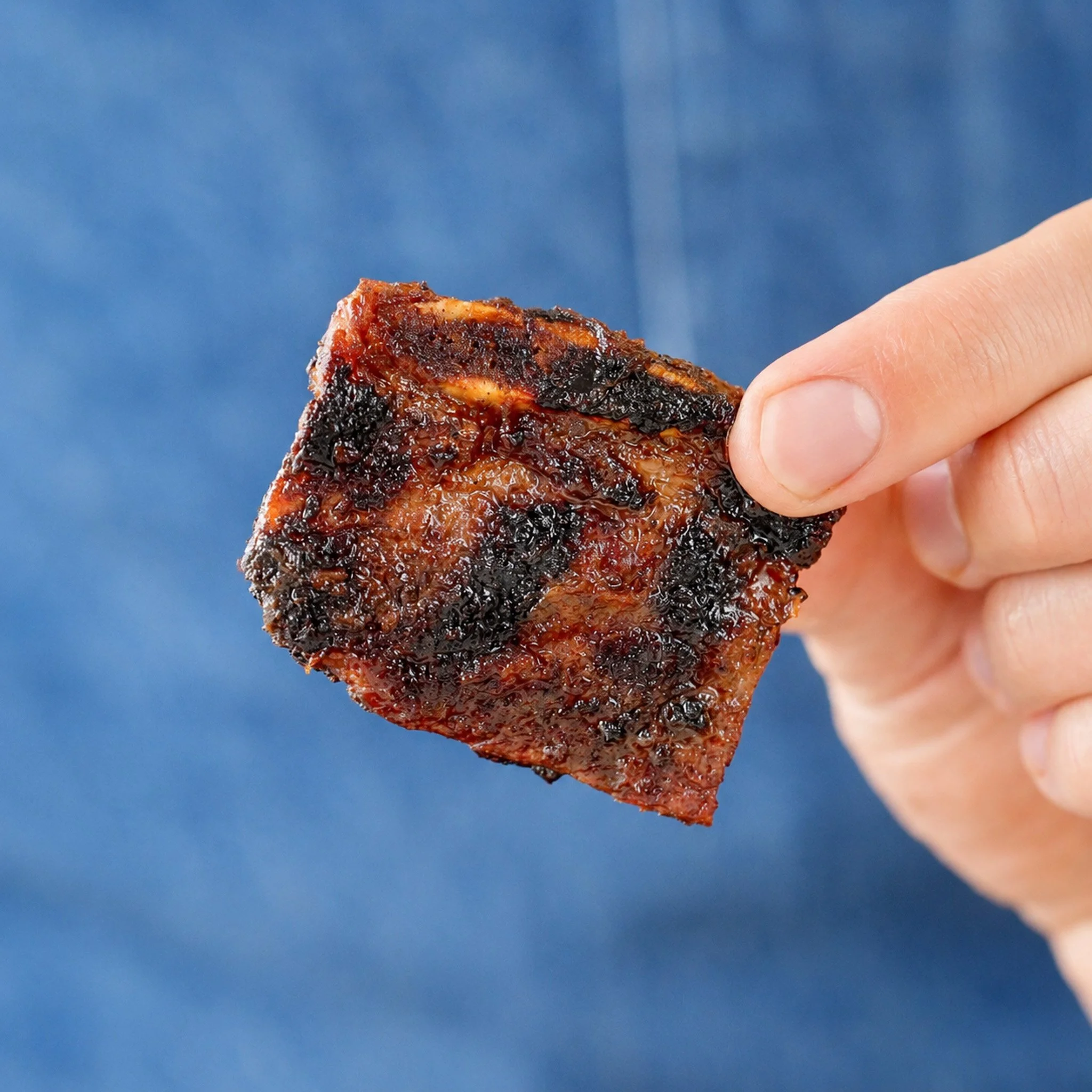 holding a piece of korean short rib with a blue apron background