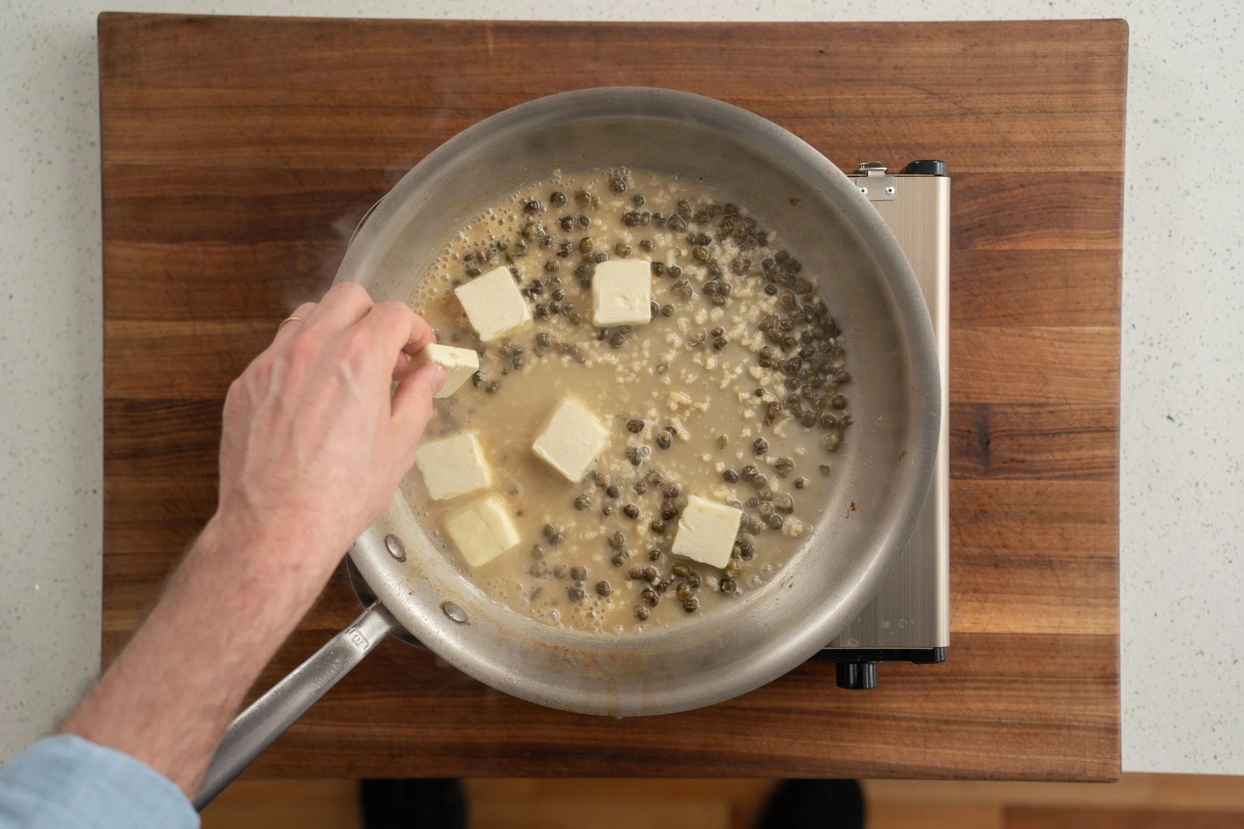adding cubed butter into white wine caper sauce