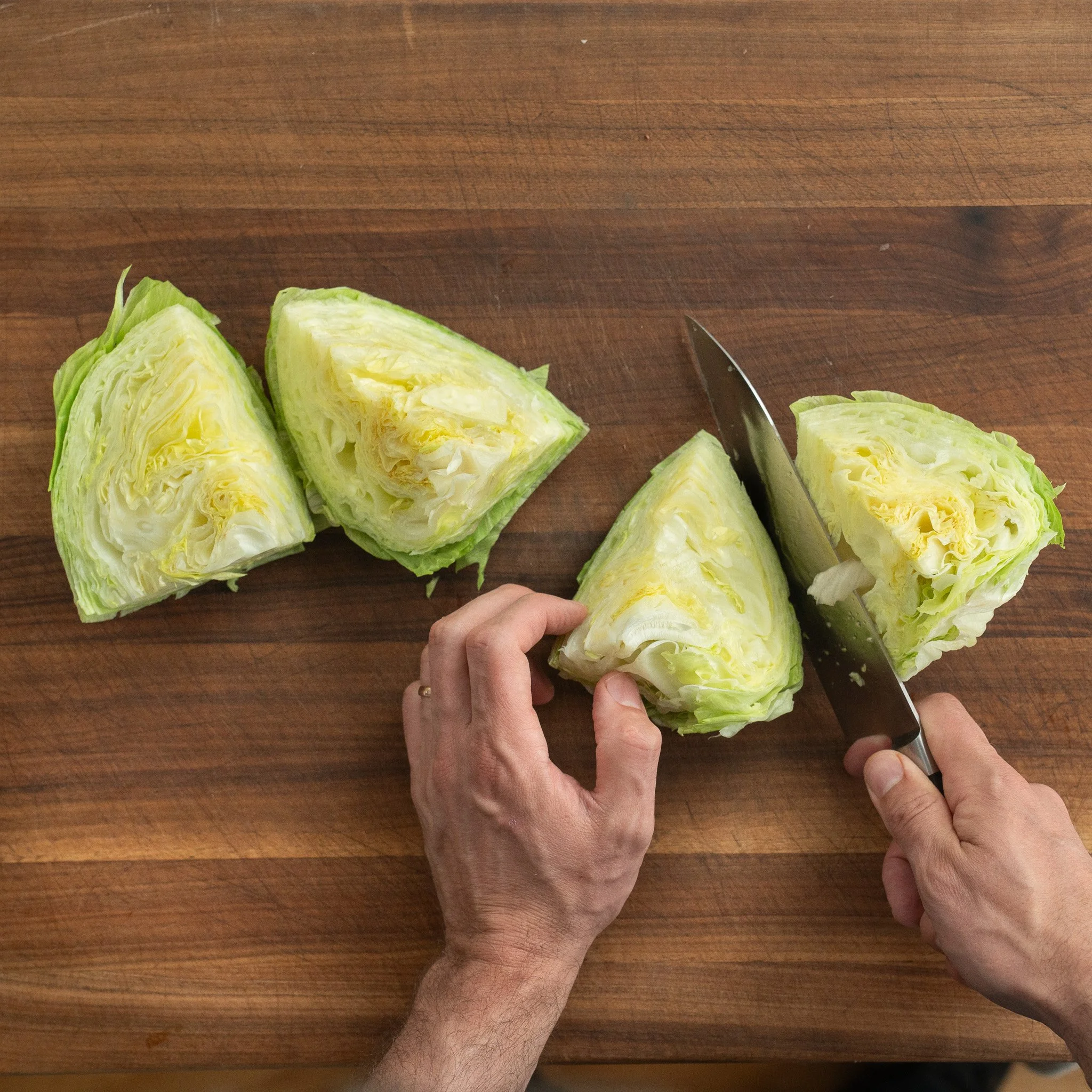 cutting iceberg lettuce into quarters on wooden cutting board