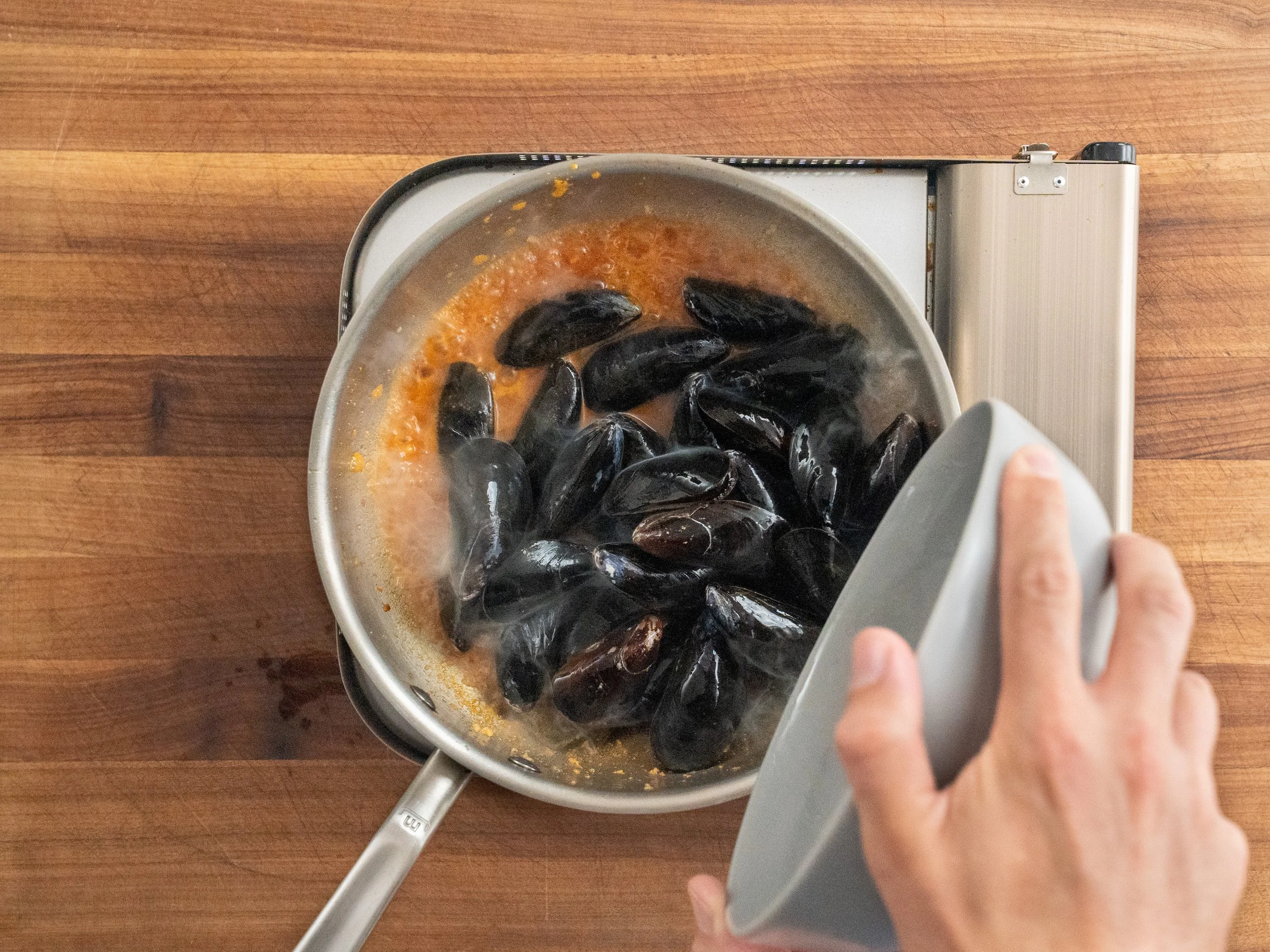 adding raw mussels into simmering silver pot of white wine sauce