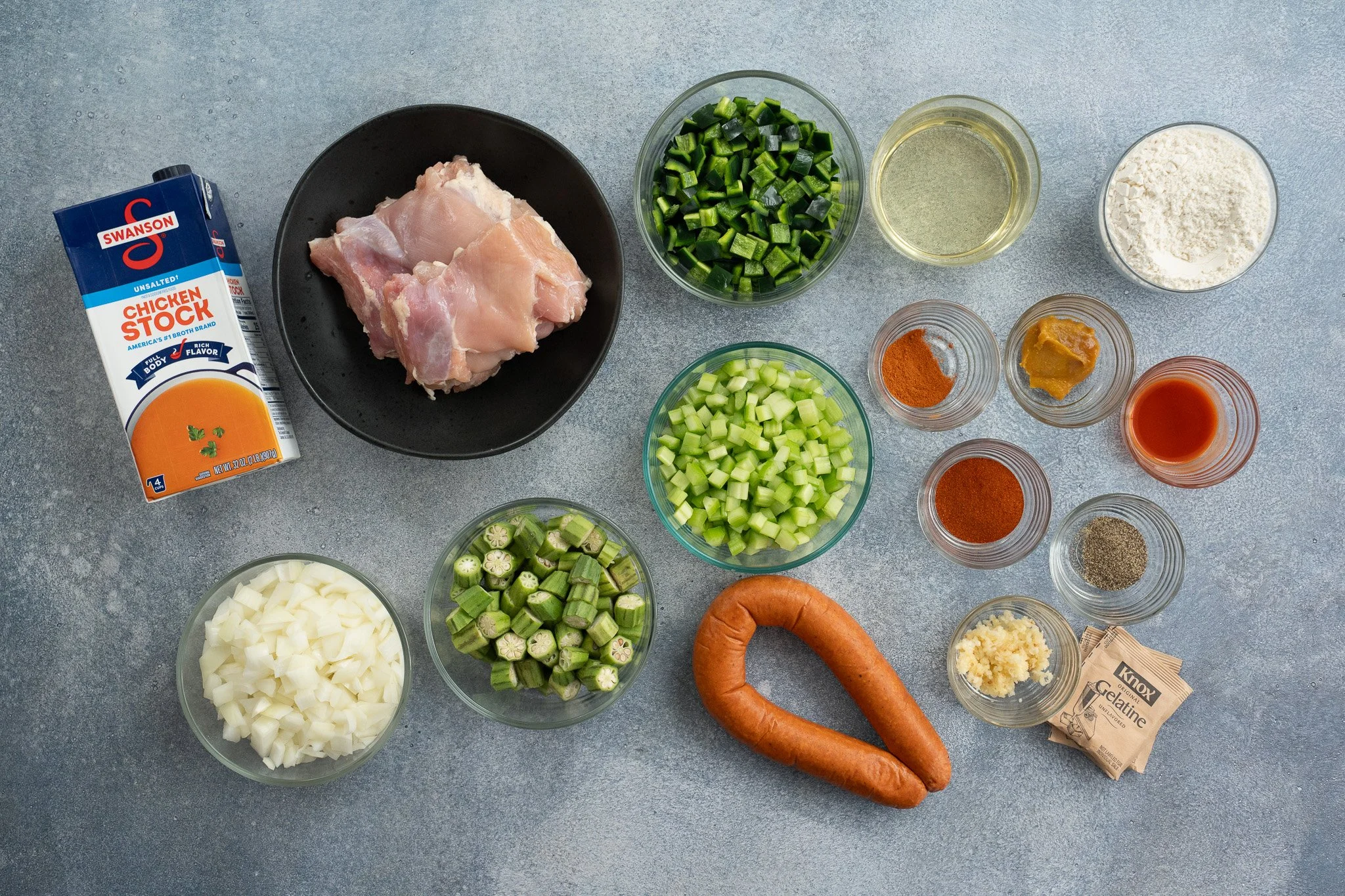 cajun gumbo ingredients in prep bowls on a grey background