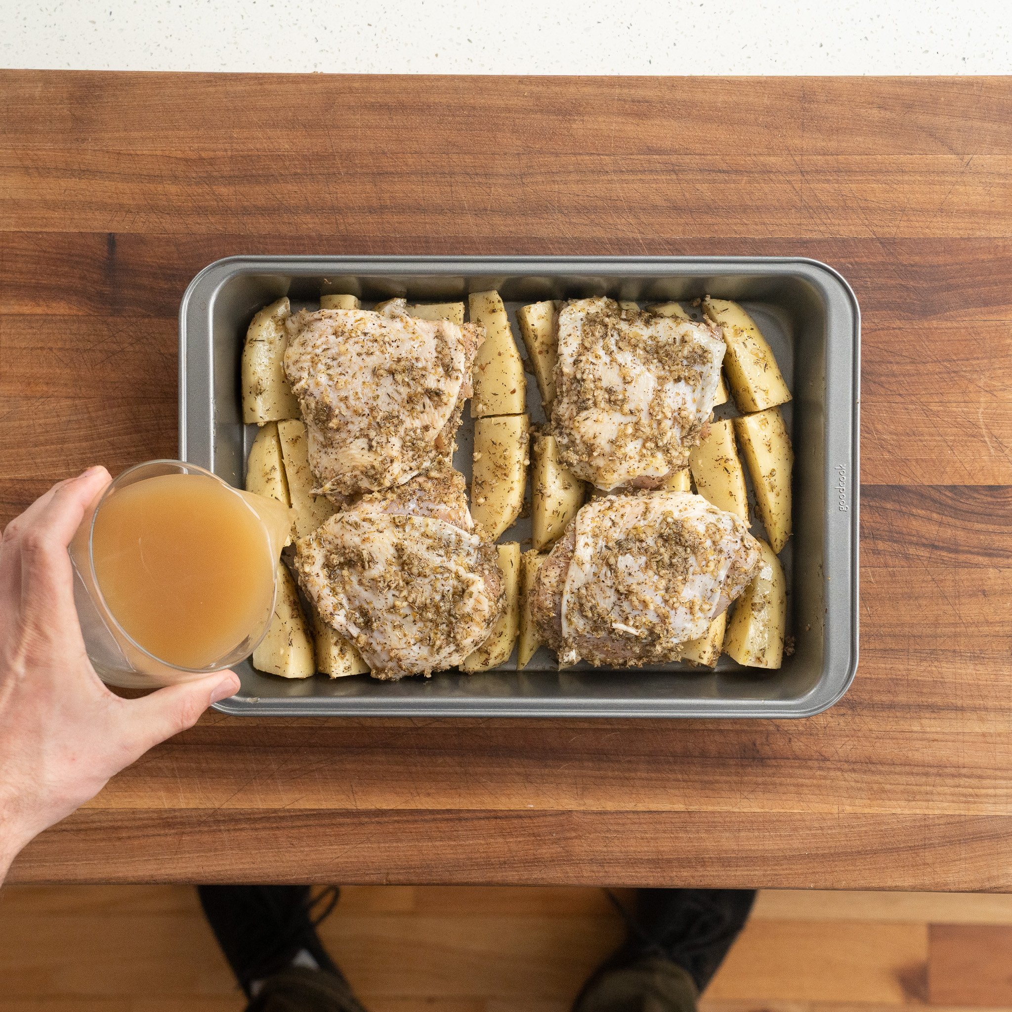 adding chicken stock to pan of potato wedges and chicken thighs