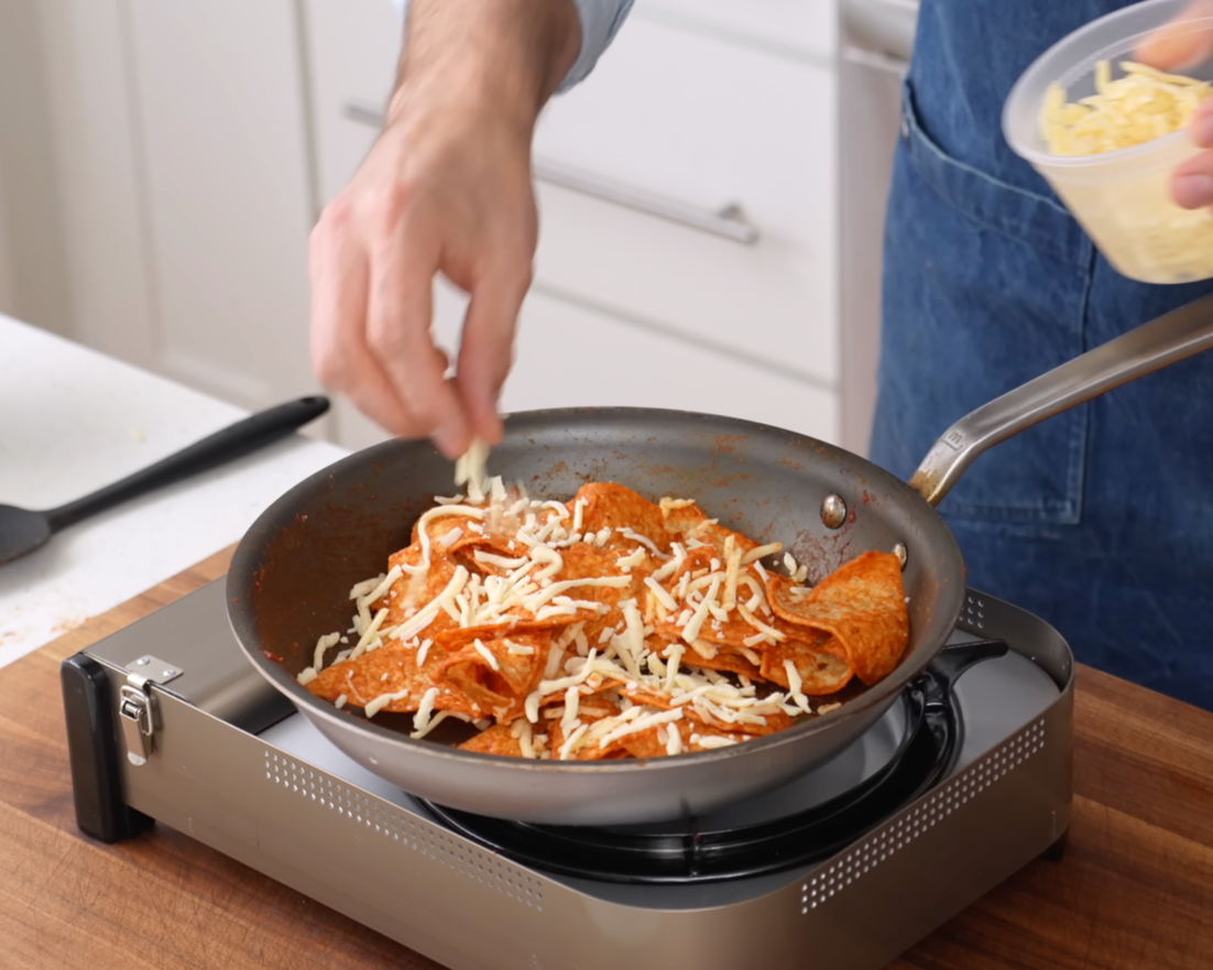 adding shredded cheese to chilaquiles