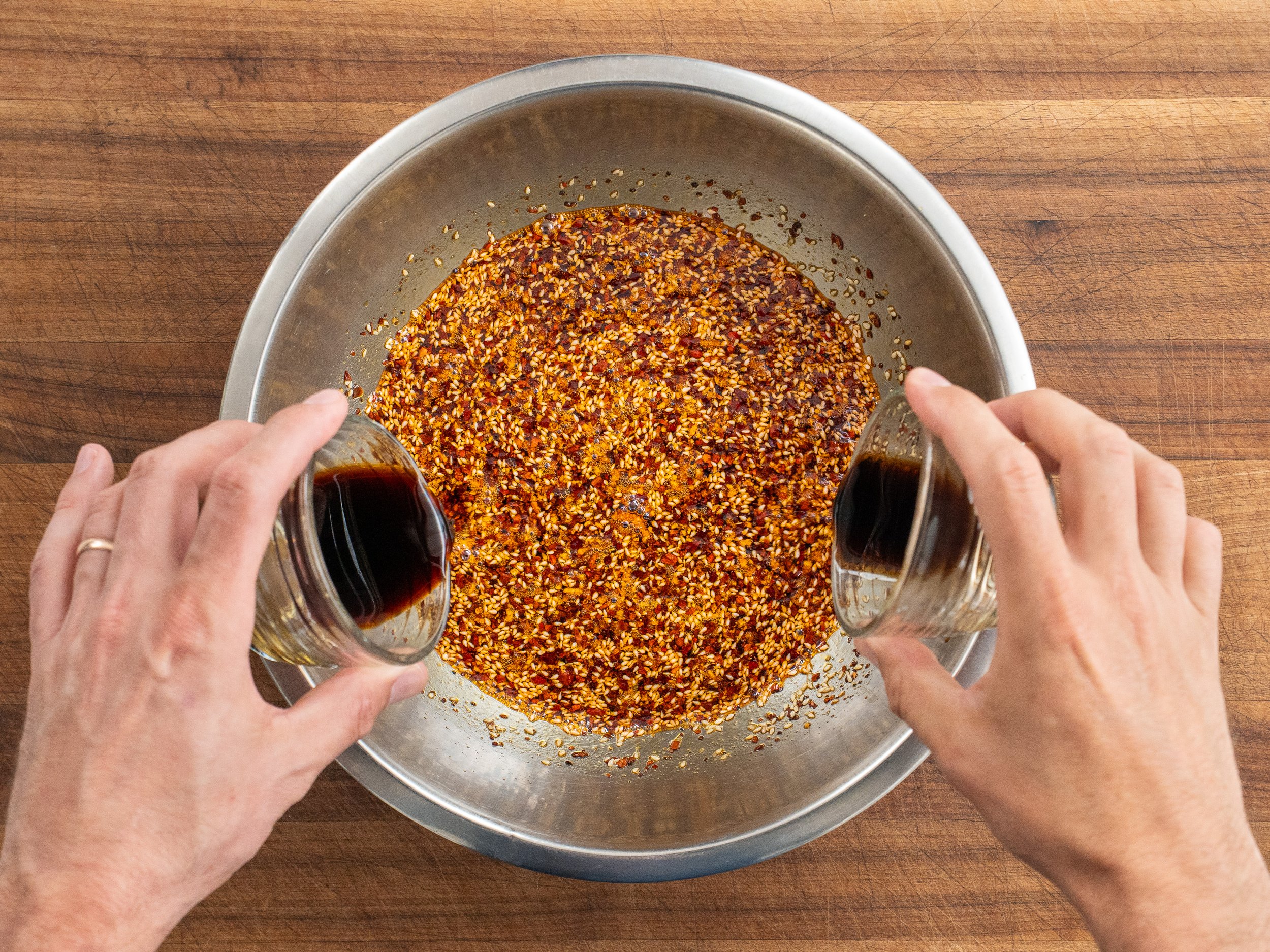 adding brown liquids into a silver bowl of spices