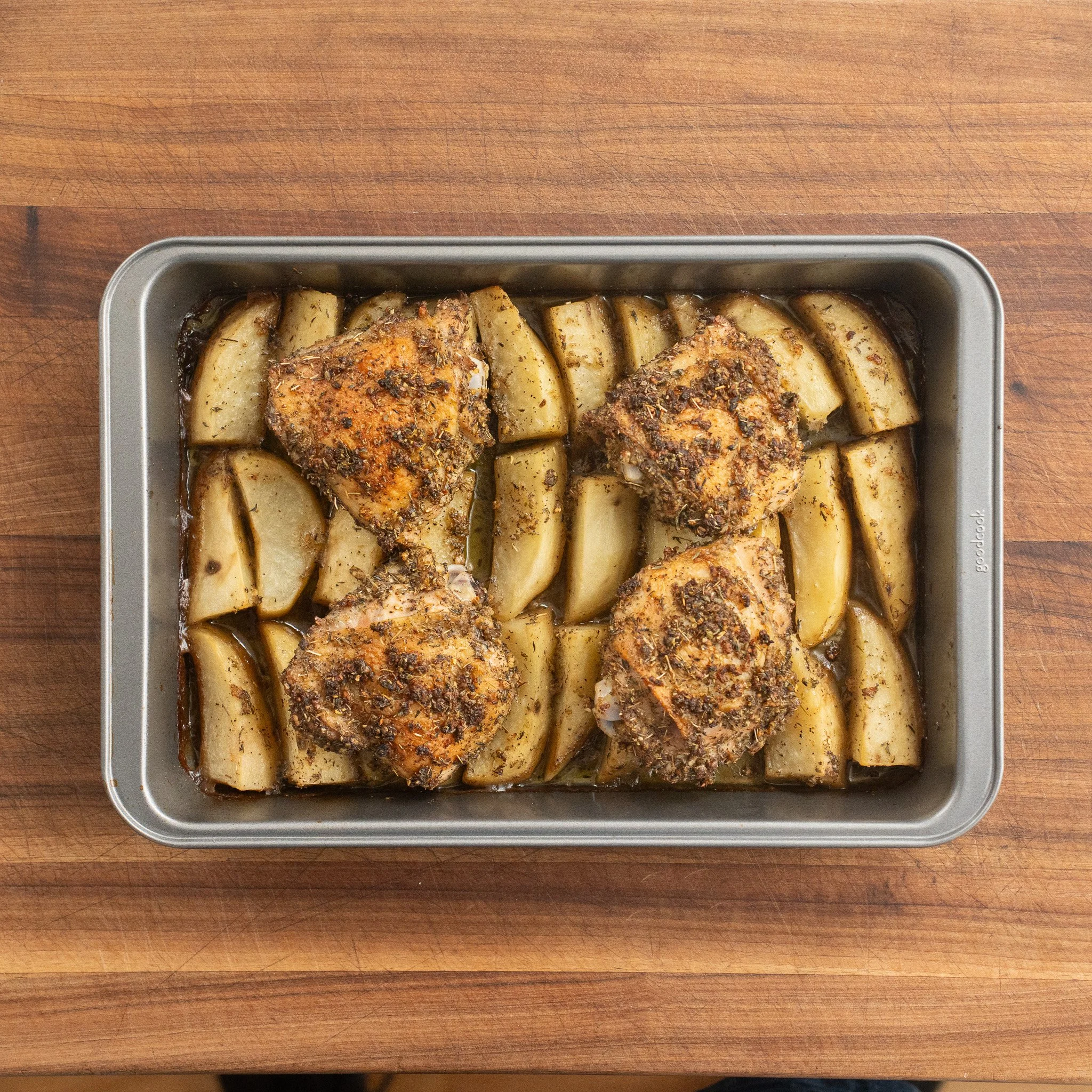 greek roast chicken thighs and potatoes in a metal pan