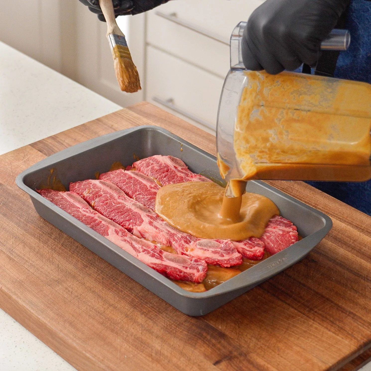 pouring galbi marinade over korean short ribs in baking pan