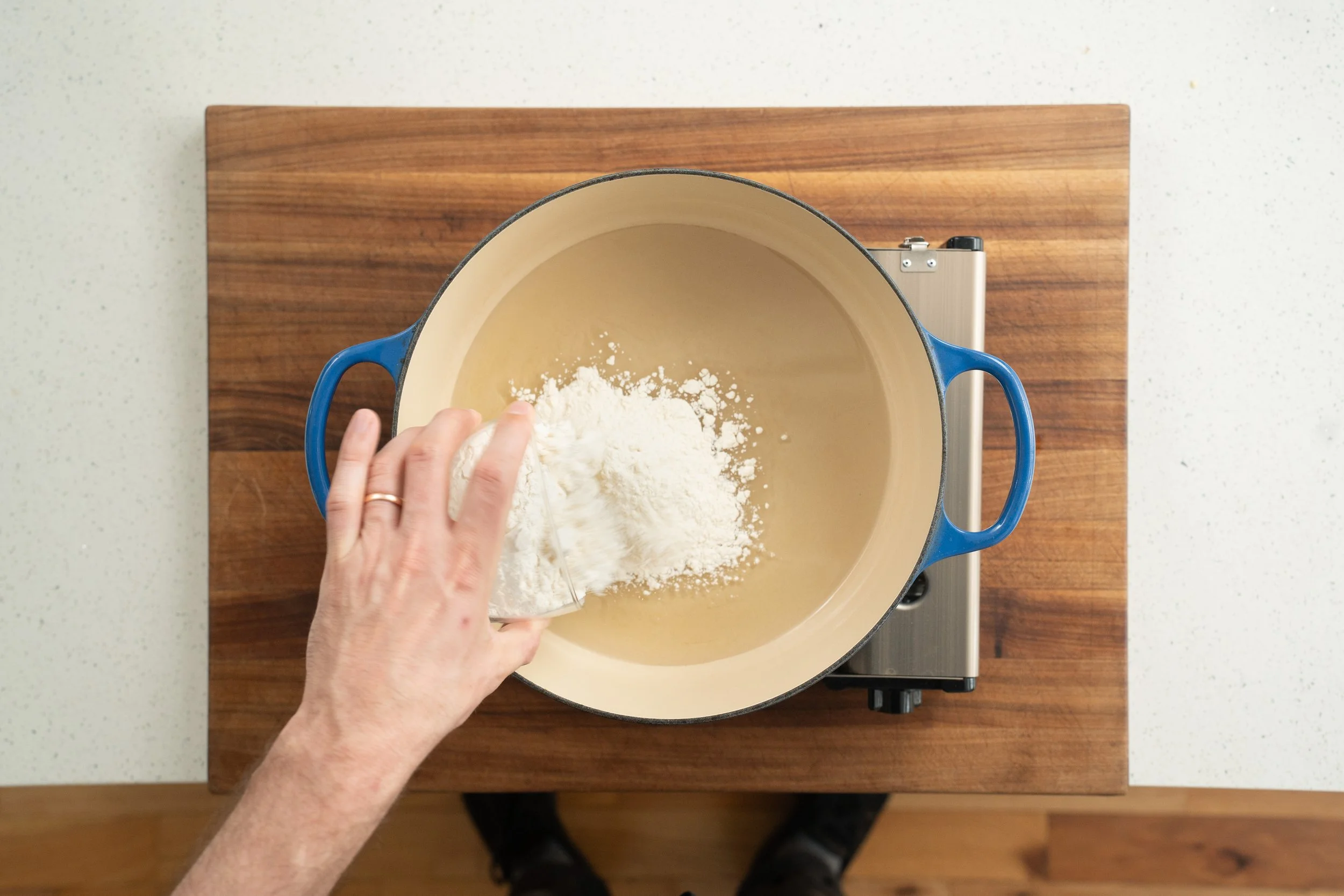 adding flour into oil in a blue dutch oven