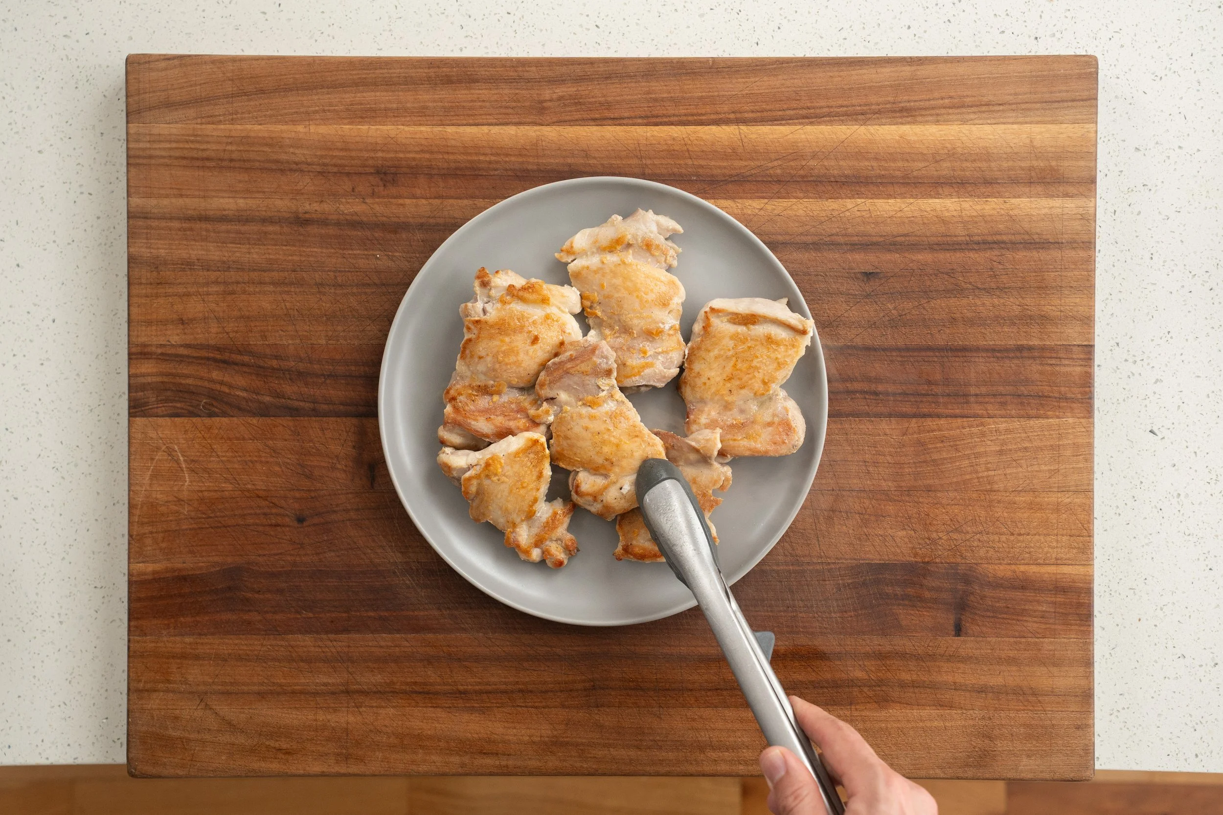 browned chicken thighs on a grey plate with tongs