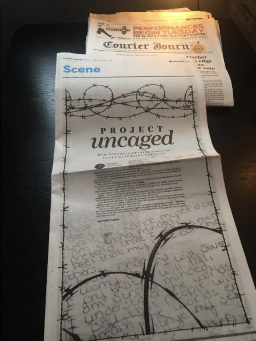 A long newspaper page titled 'PROJECT uncaged' with barbed wire illustrations and handwritten text visible at the bottom, with additional newspapers stacked behind it.