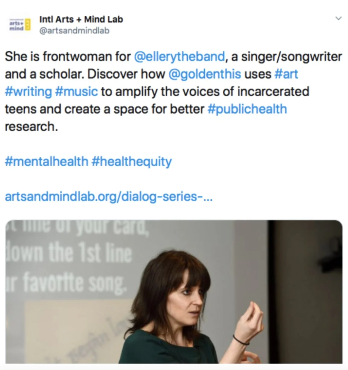 A woman (Dr. Tasha Golden) with dark brown hair speaking to an audience, with a slide behind her displaying text from her presentation.