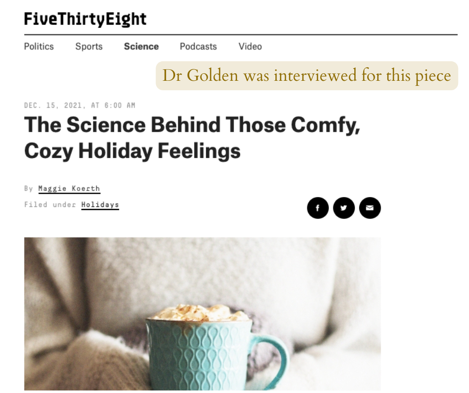 A webpage titled 'The Science Behind Those Comfy, Cozy Holiday Feelings' featuring an article about holiday comfort (in which Dr. Tasha Golden is interviewed) and a picture of a person holding a mug with a warm beverage, wearing a beige sweater.