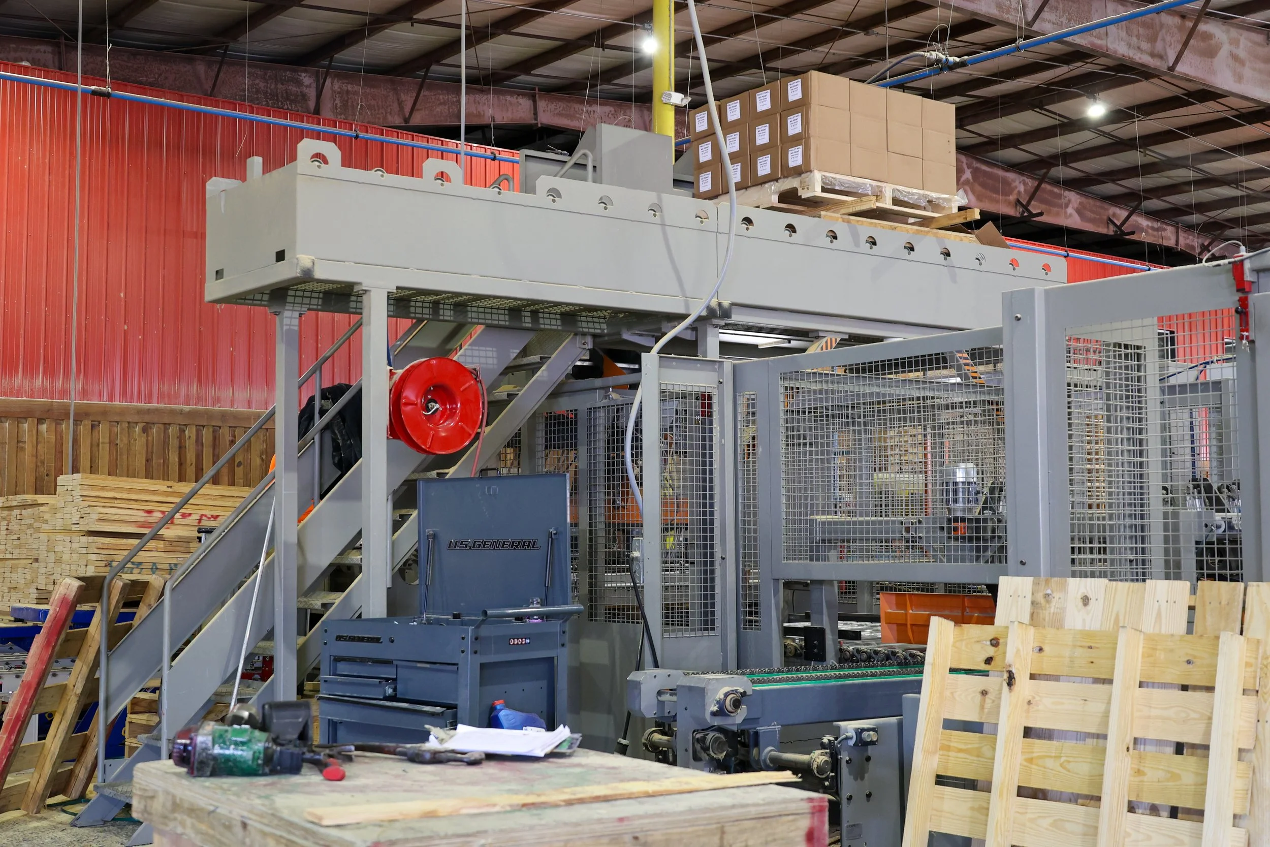 Industrial woodworking manufacturing machine in a factory, with wooden pallets and crates nearby.