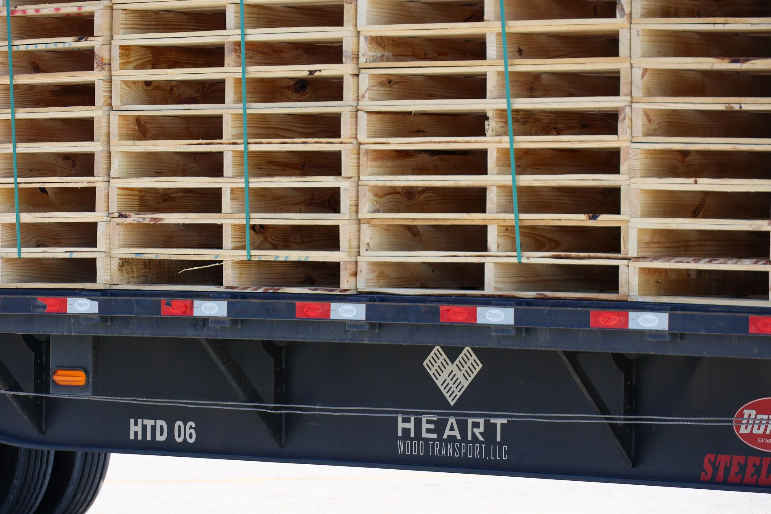 A flatbed truck with a load of stacked empty wooden pallets.