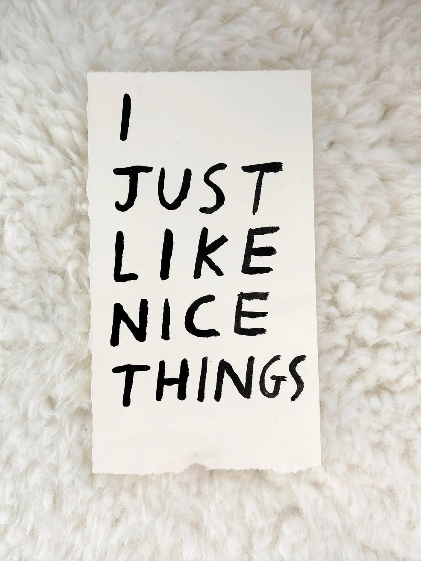 A white paper with black handwritten text that reads "I just like nice things" on a fluffy white surface.