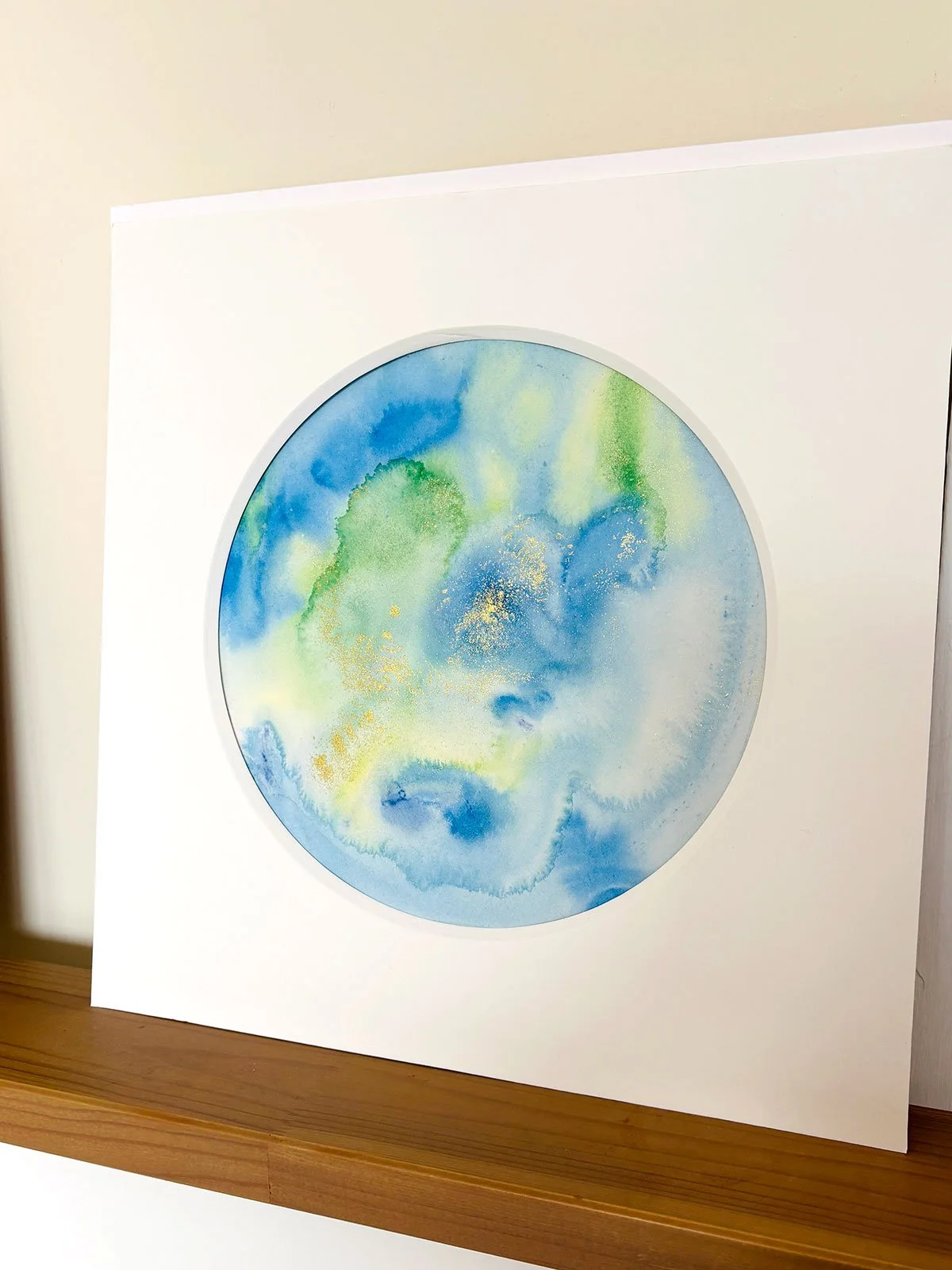 Abstract watercolour painting in varying tones of green, yellow, blue and gold sparkles.
