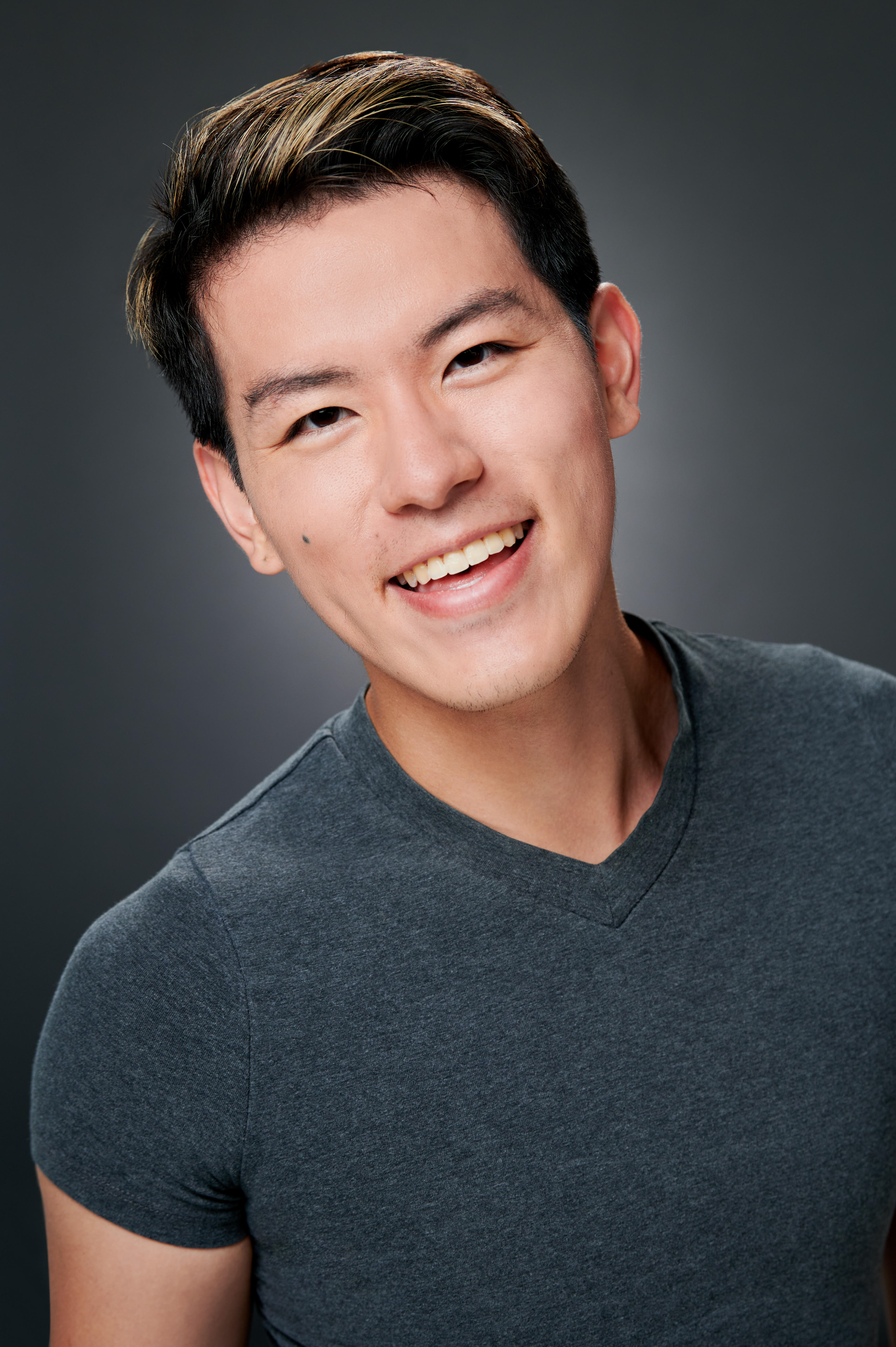 Asian American man smiles in gray V neck tee
