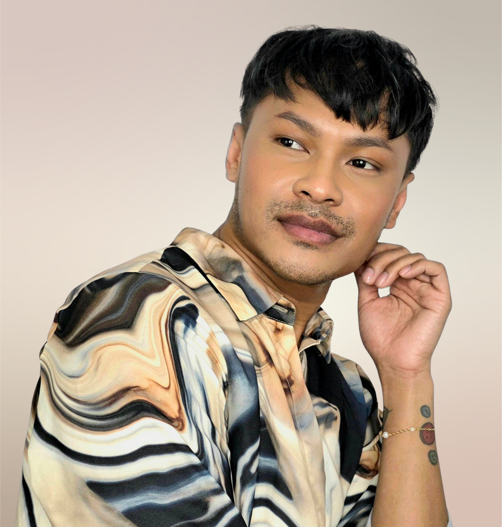 Asian American male dancer poses with head on hand, wearing a shirt with swirl designs