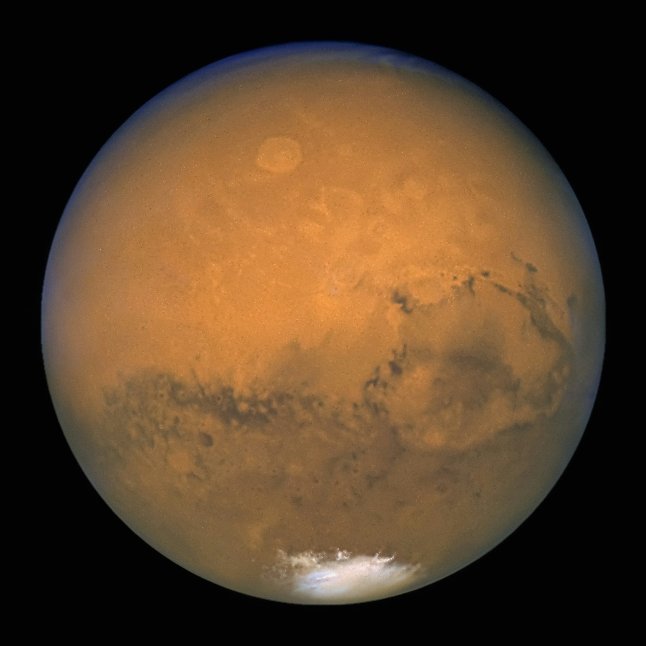 Close-up of the planet Mars showing its reddish surface with dark volcanic features and polar ice cap.