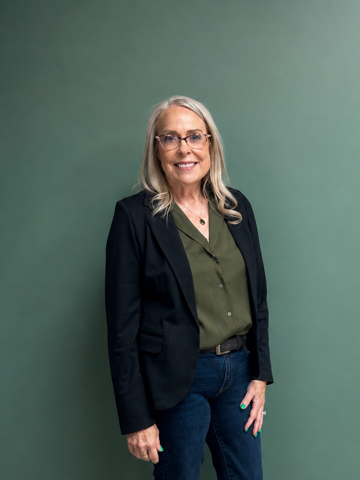 Merit KC's Pam Stands Smiling in a green shirt and jeans against a green accent wall