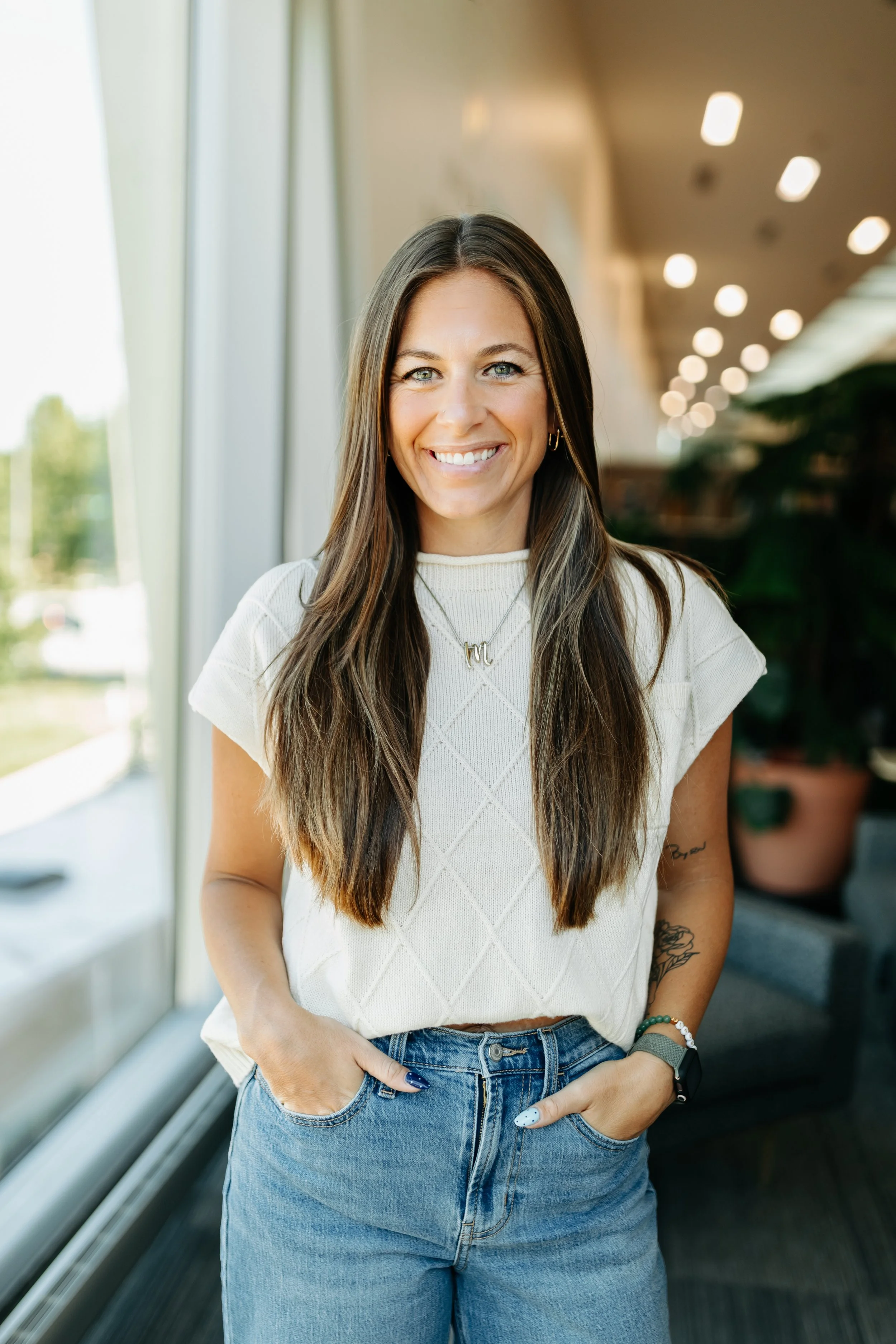 Merit Weigh Loss & Wellness RN, Lauren, Stands smiling with her hands tucked in her jeans in a white shirt in a well lit room.