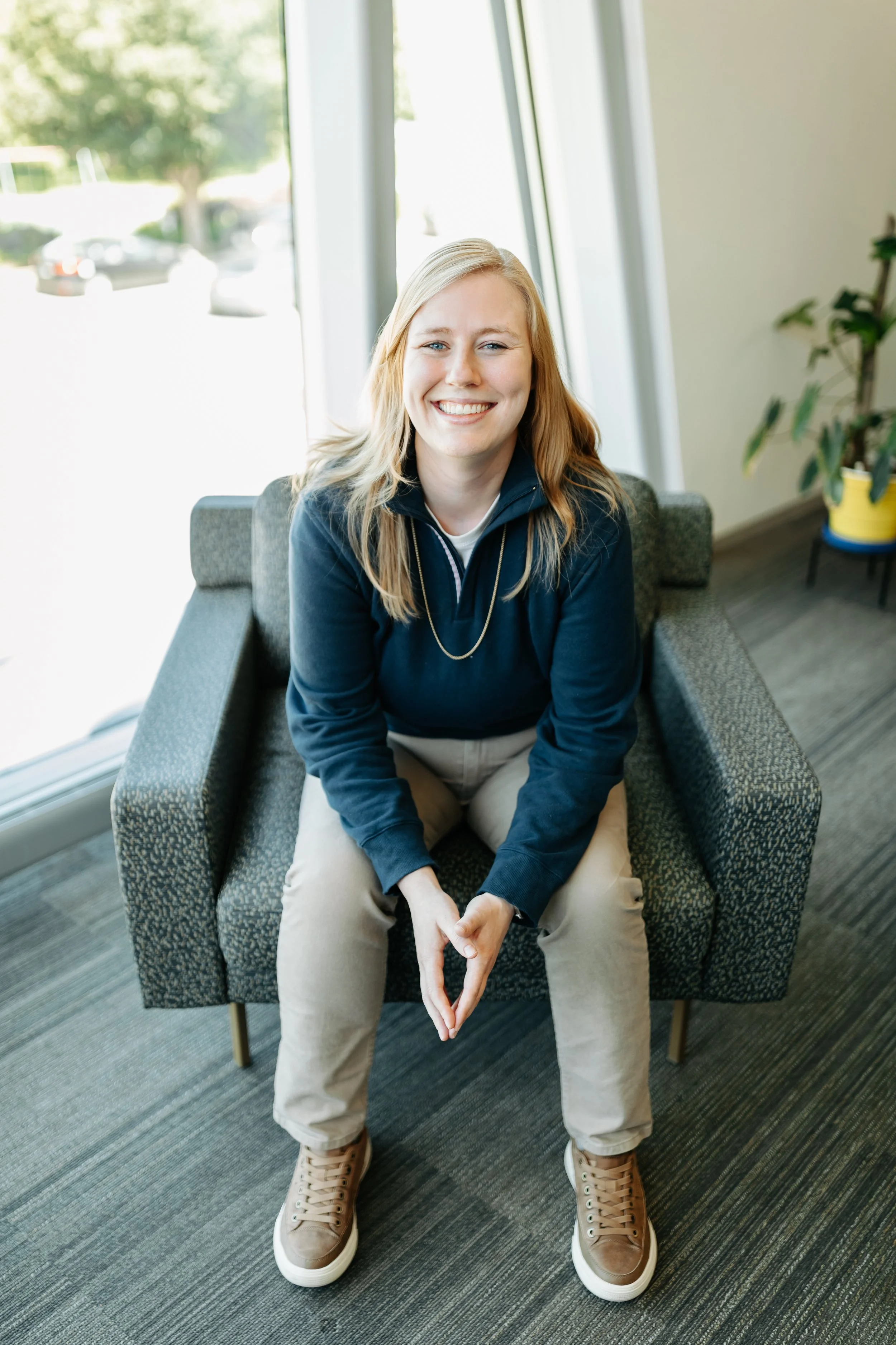 Merit Weight Loss & Wellness Marketing & Growth manager Rachel sits in a blue sweater with blonde hair smiling with her hands touching in her lap