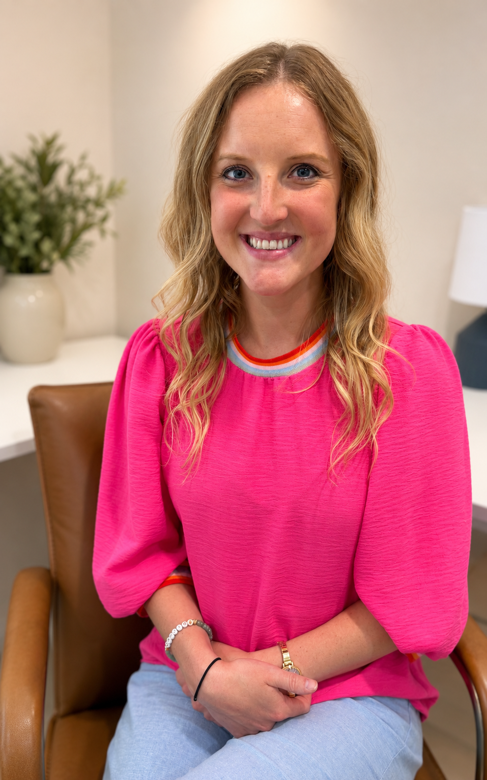 Merit Topeka's APRN Britnee sits in a pink shirt with her hands crossed smiling