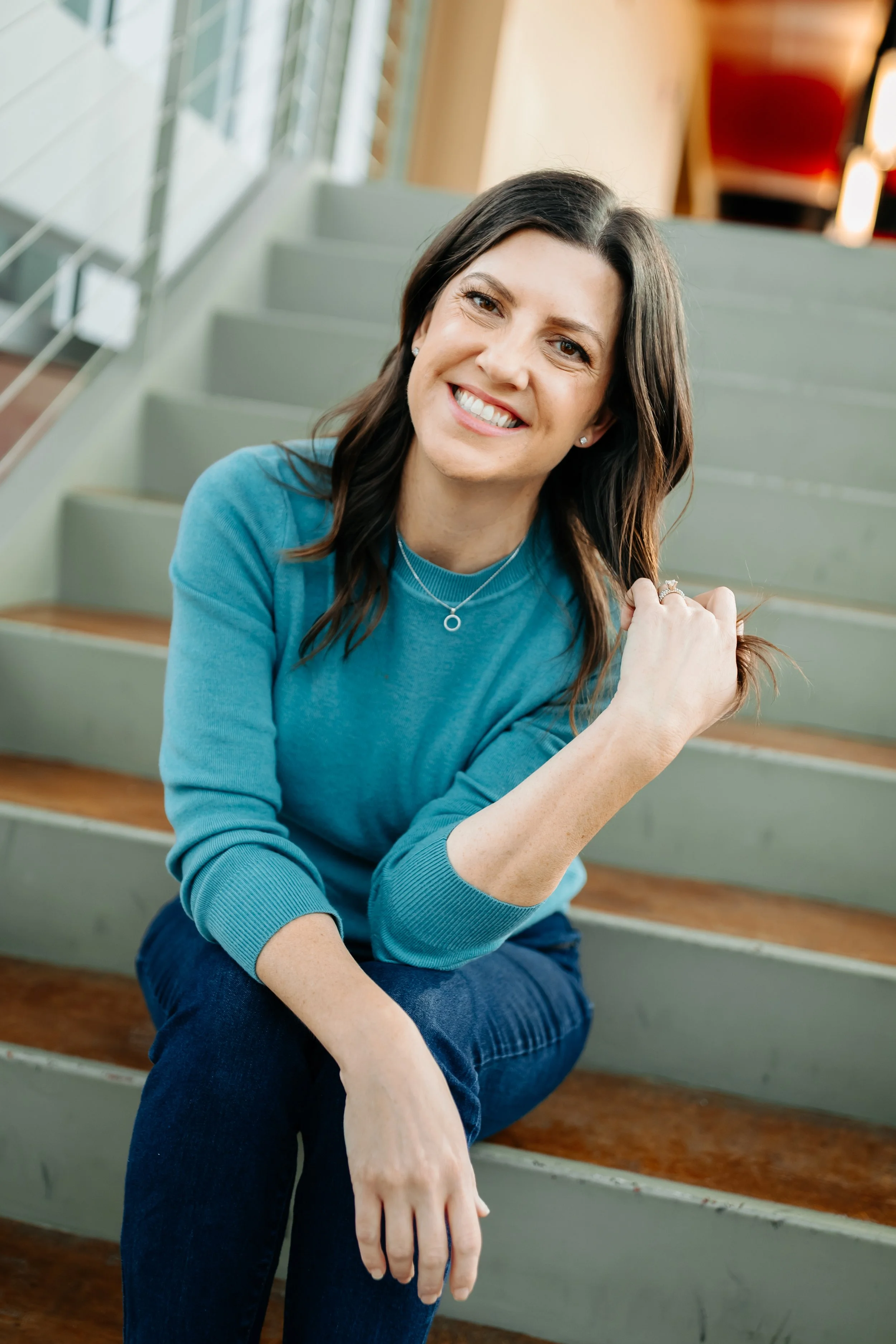 Merit Owner, Stephanie, sits on stairs smiling with a hand in her hair