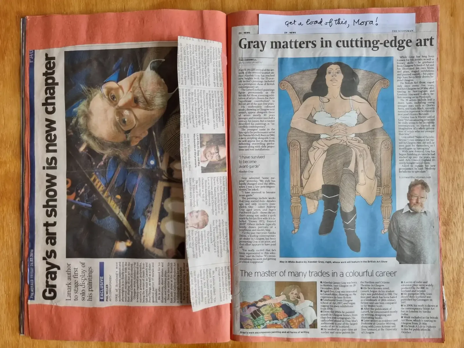 An open scrapbook of newspaper pages about Alasdair's art, including his drawing of a woman seated in an armchair. A slip of paper at the top reads, in handwriting, 'Get a load of this, Mora!'