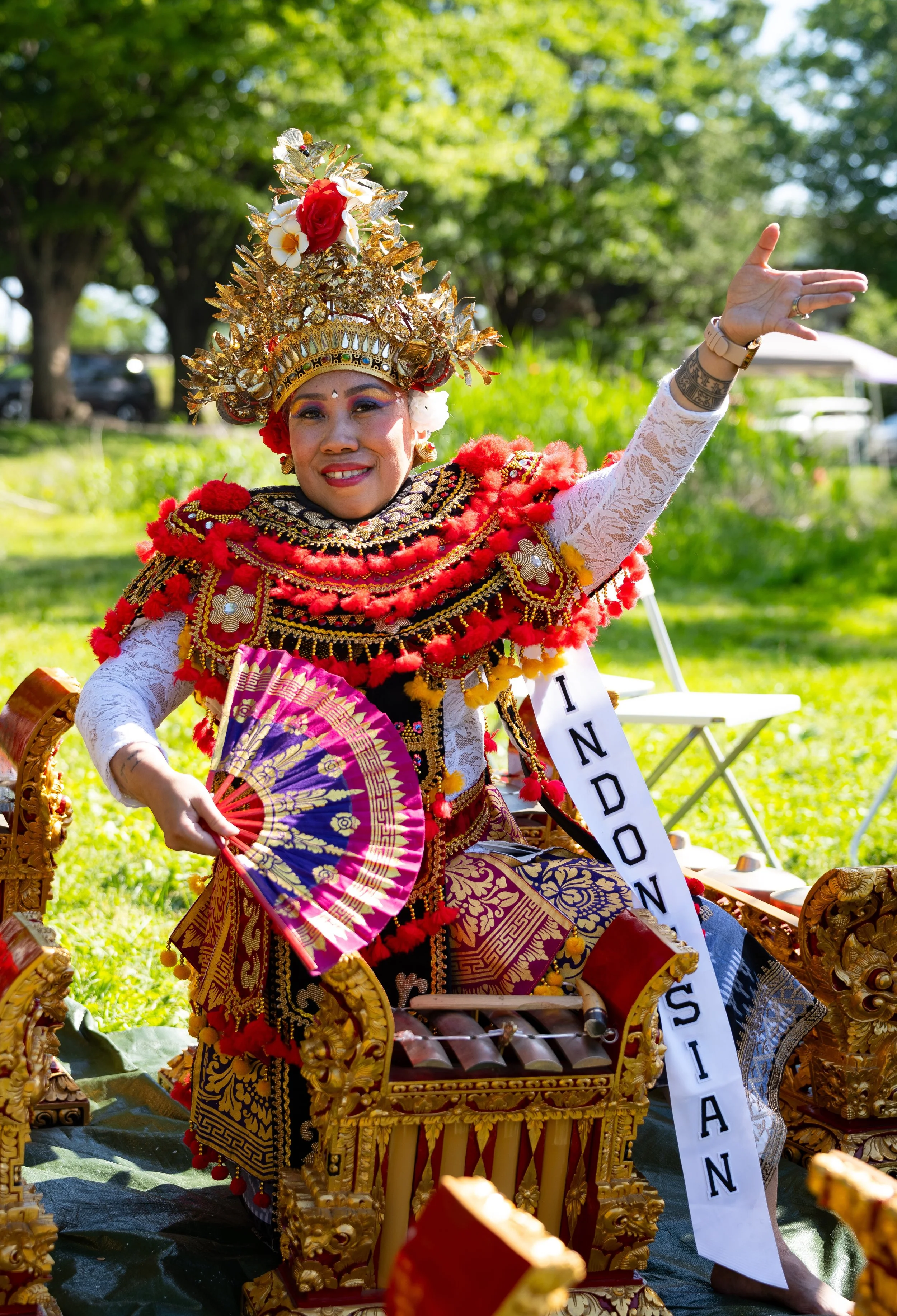 A woman dressed in traditional, colorful Indonesian dance costume performing a graceful dance indoors.