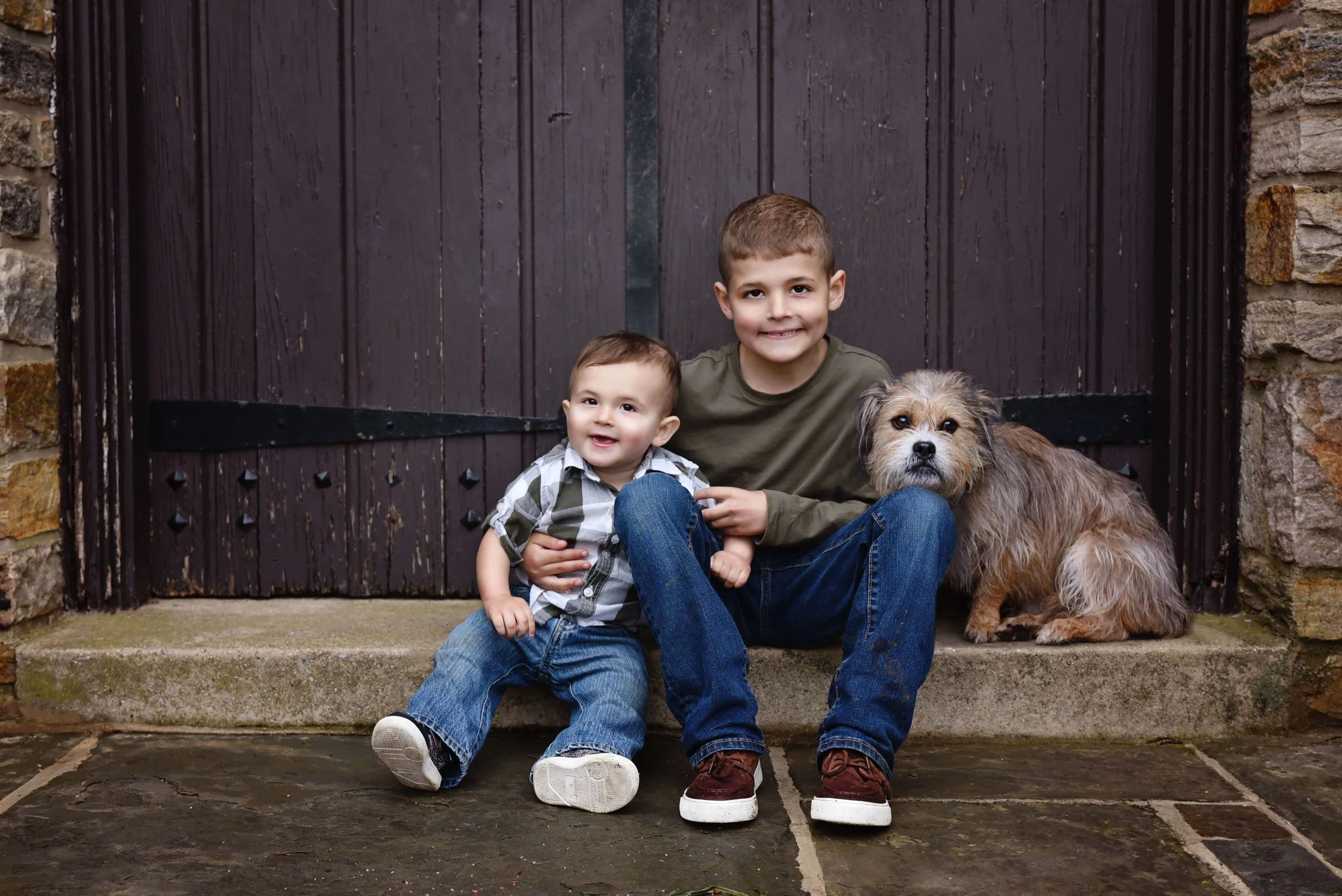 Two young brothers sitting together with their family dog during an outdoor family portrait session in Shenandoah County, Virginia 