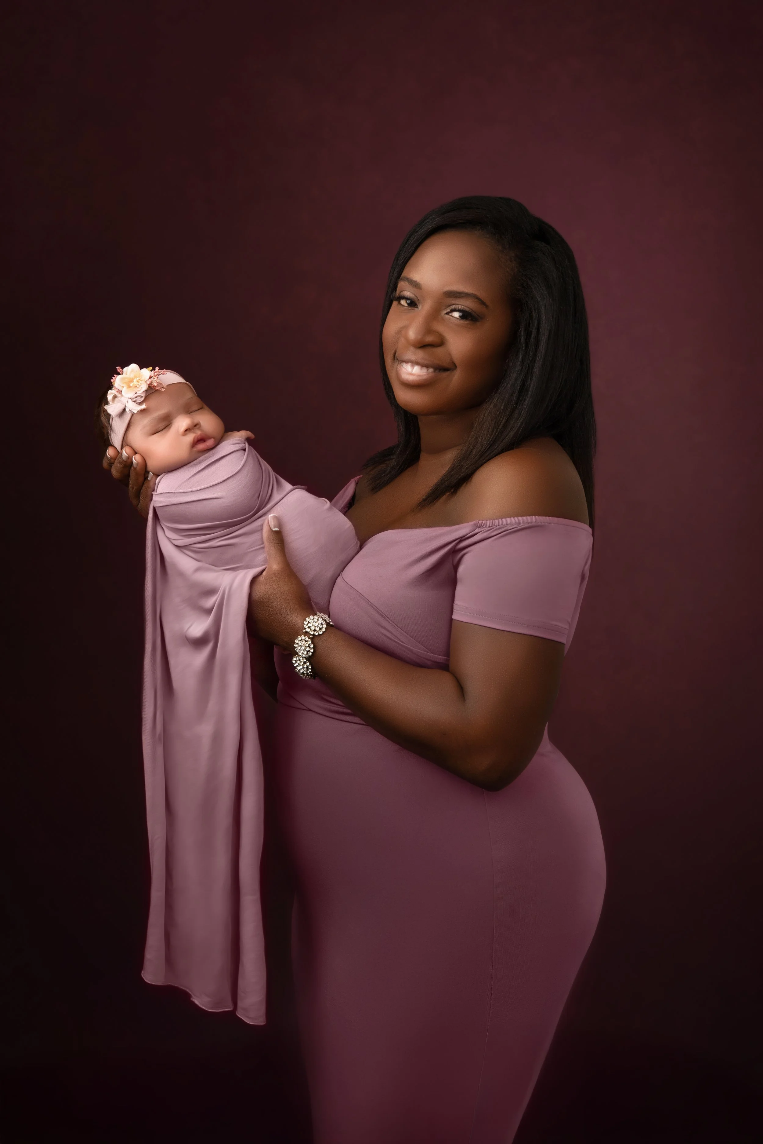 Mother holding her newborn baby during a studio portrait session in Woodstock, Virginia, both dressed in coordinating mauve tones. 